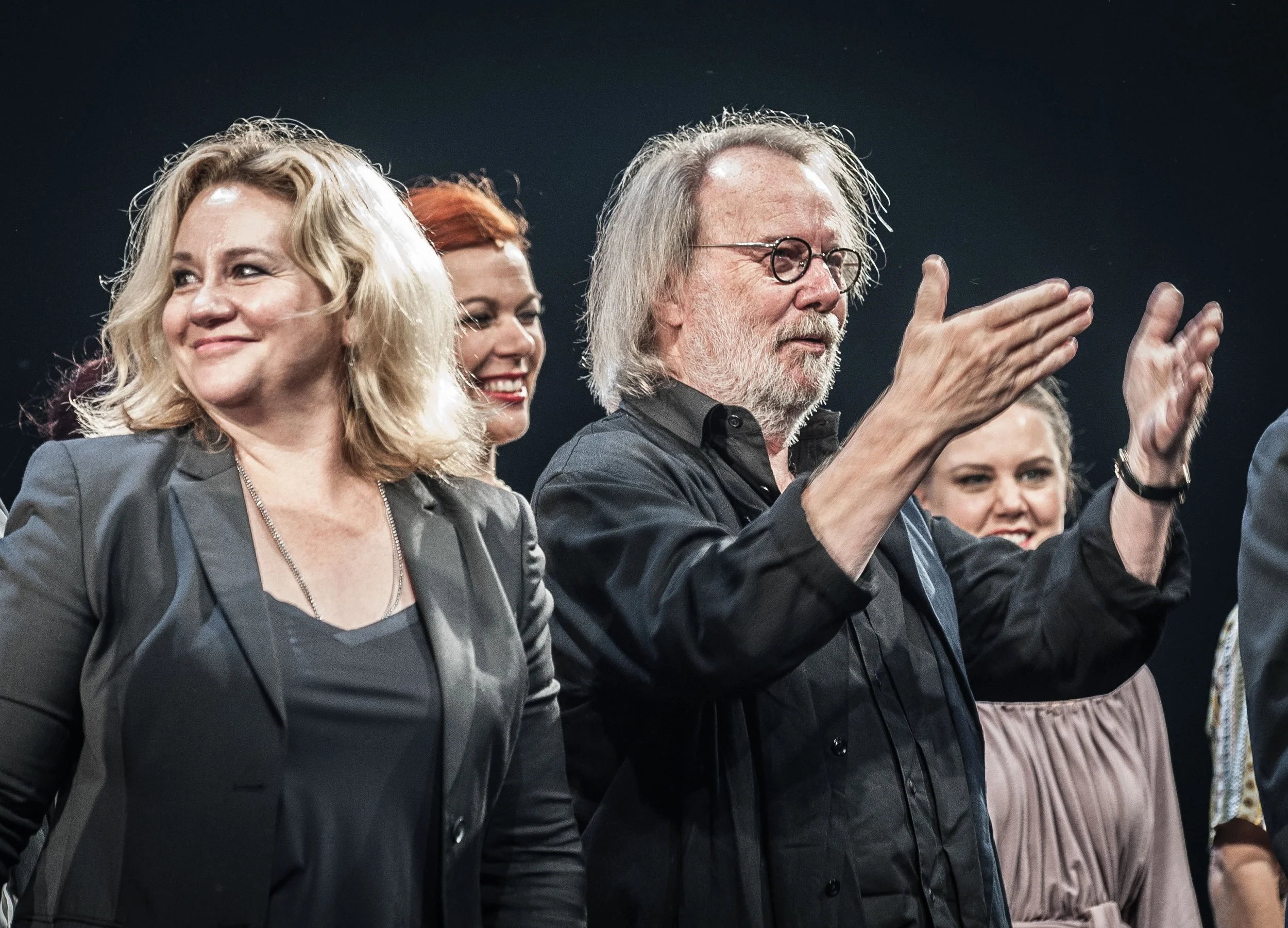 Group of people standing together, some clapping, at an event.