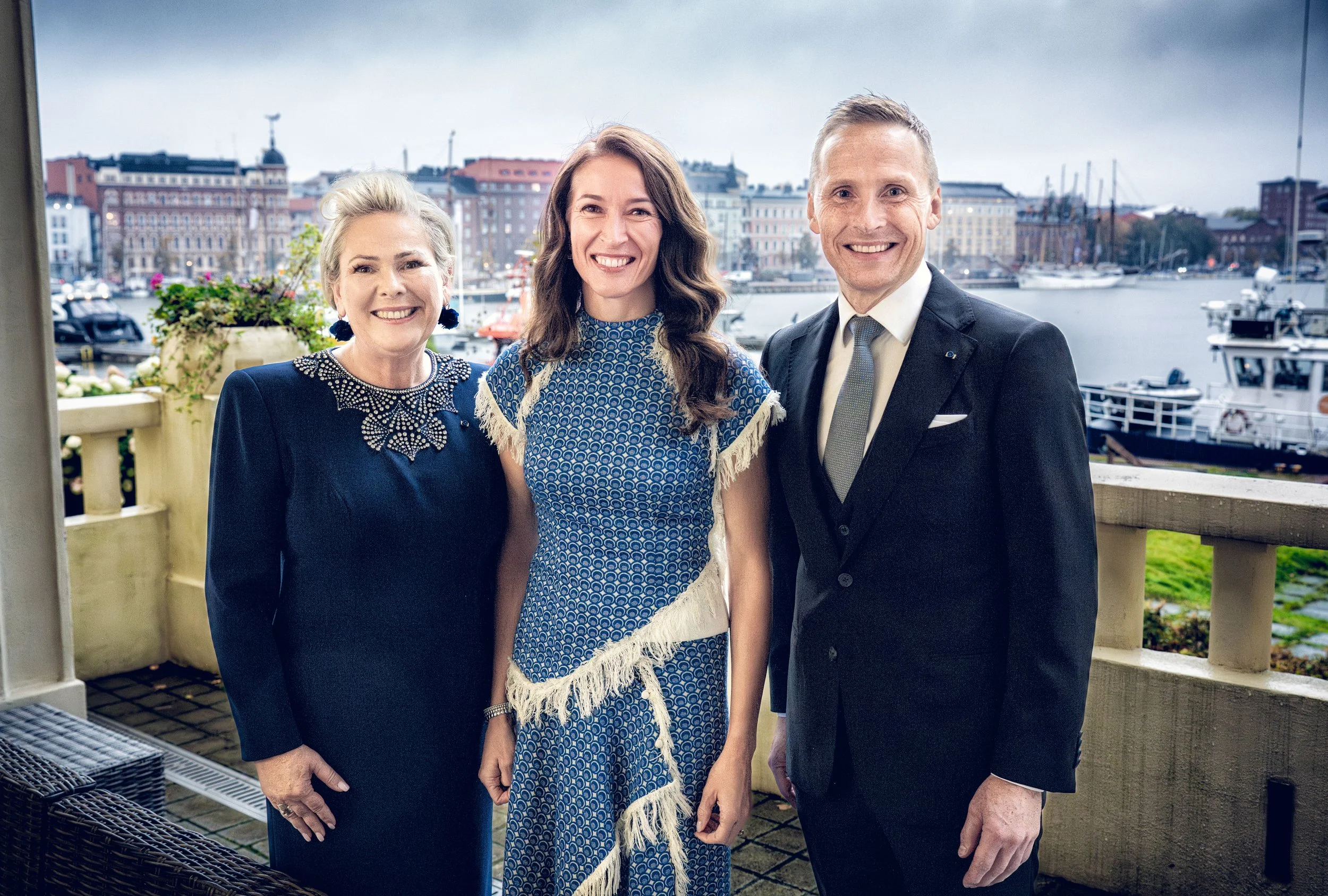 Three people standing together outdoors near a marina with boats and buildings in the background, smiling for the camera.