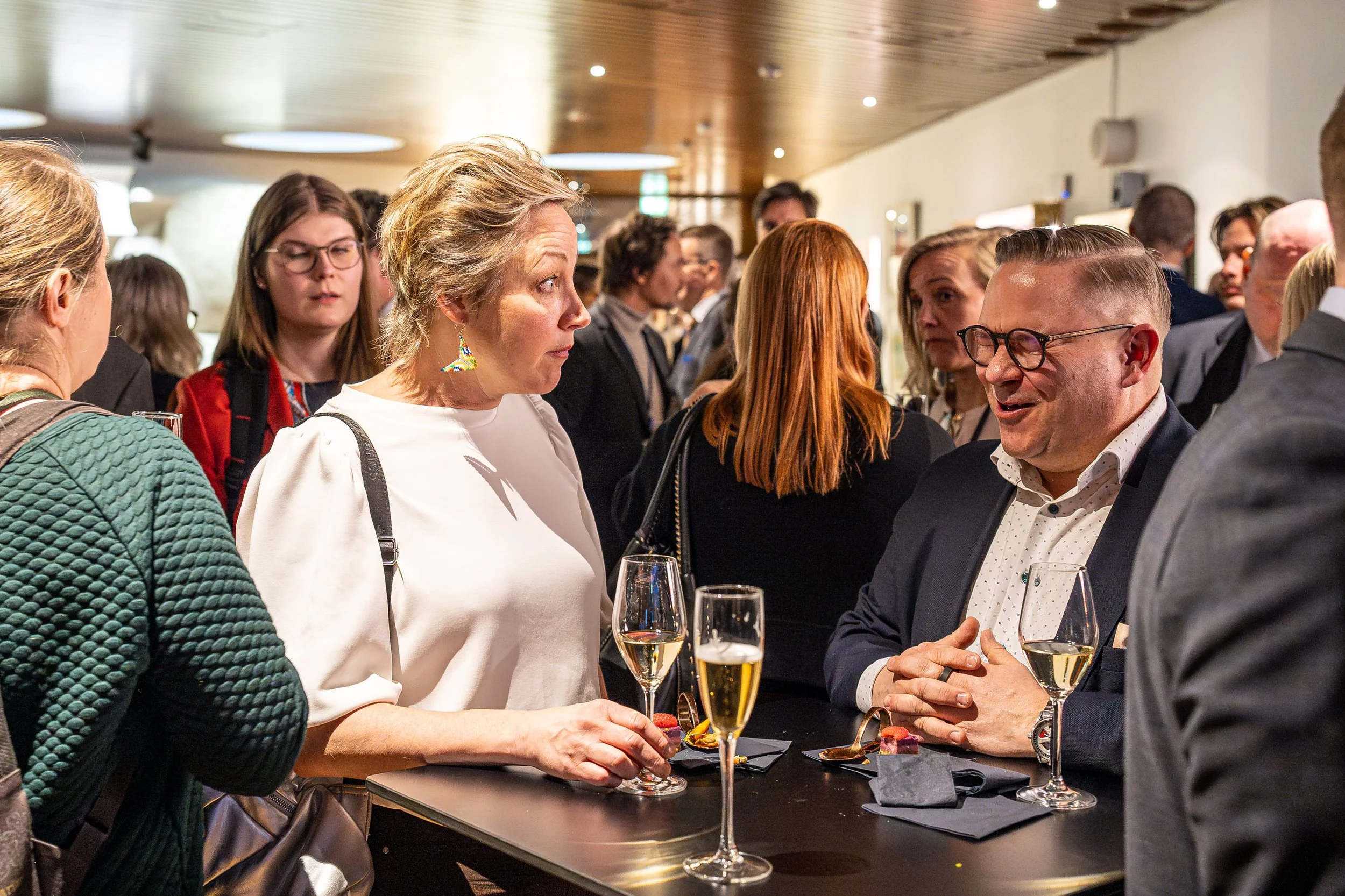 Group of people talking at a social event, holding glasses of champagne.