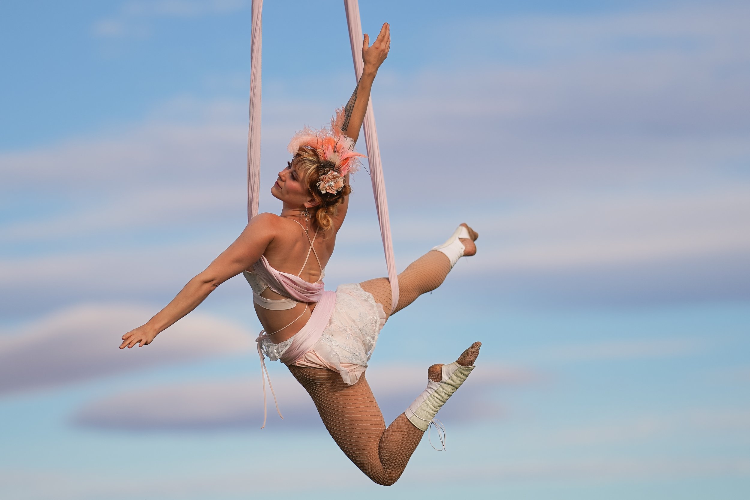 A woman dressed as a circus aerialist or acrobat performing on silk fabric outdoors.