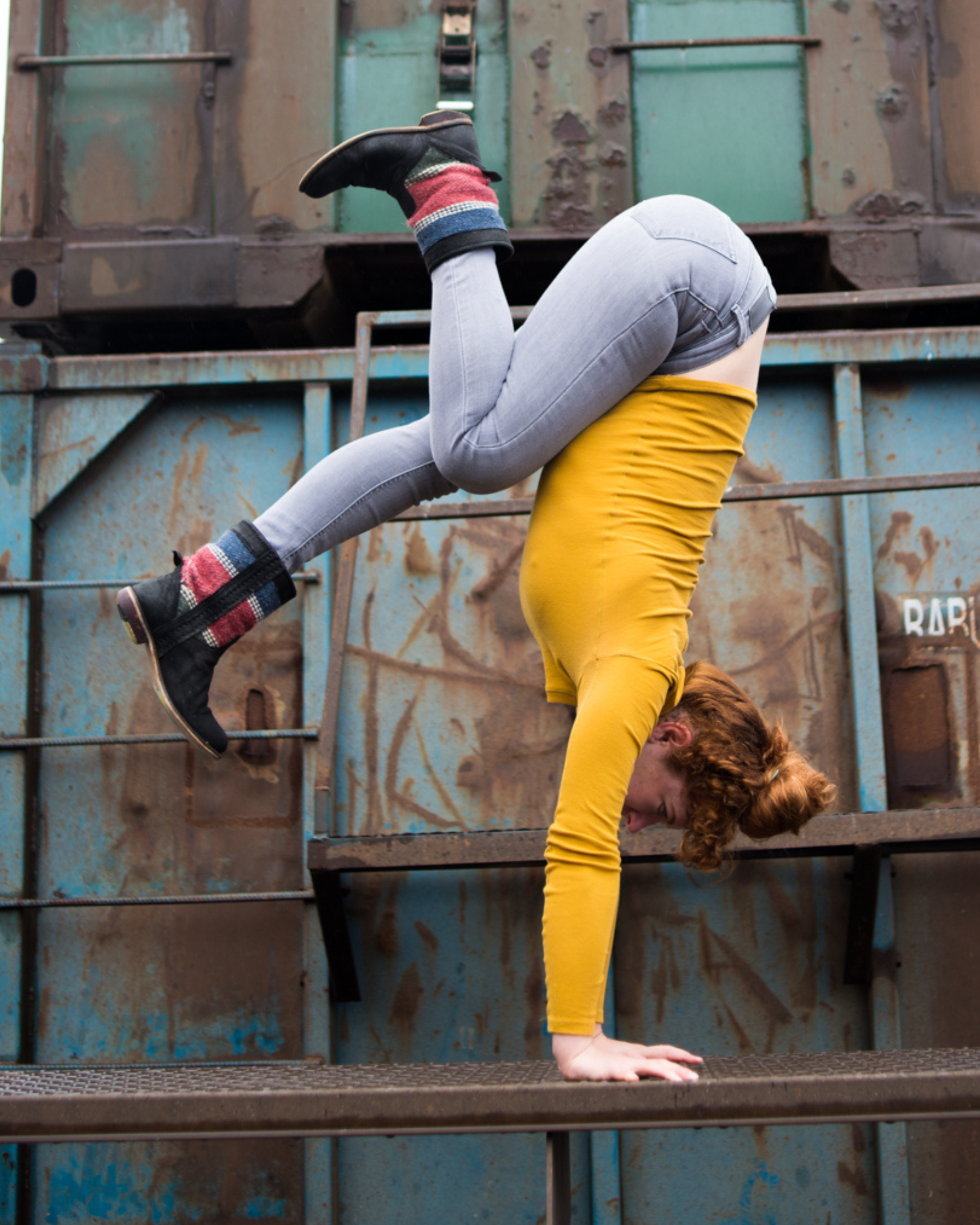 Person performing a handstand on a metal surface in an urban, industrial setting, with distressed metal walls in the background.
