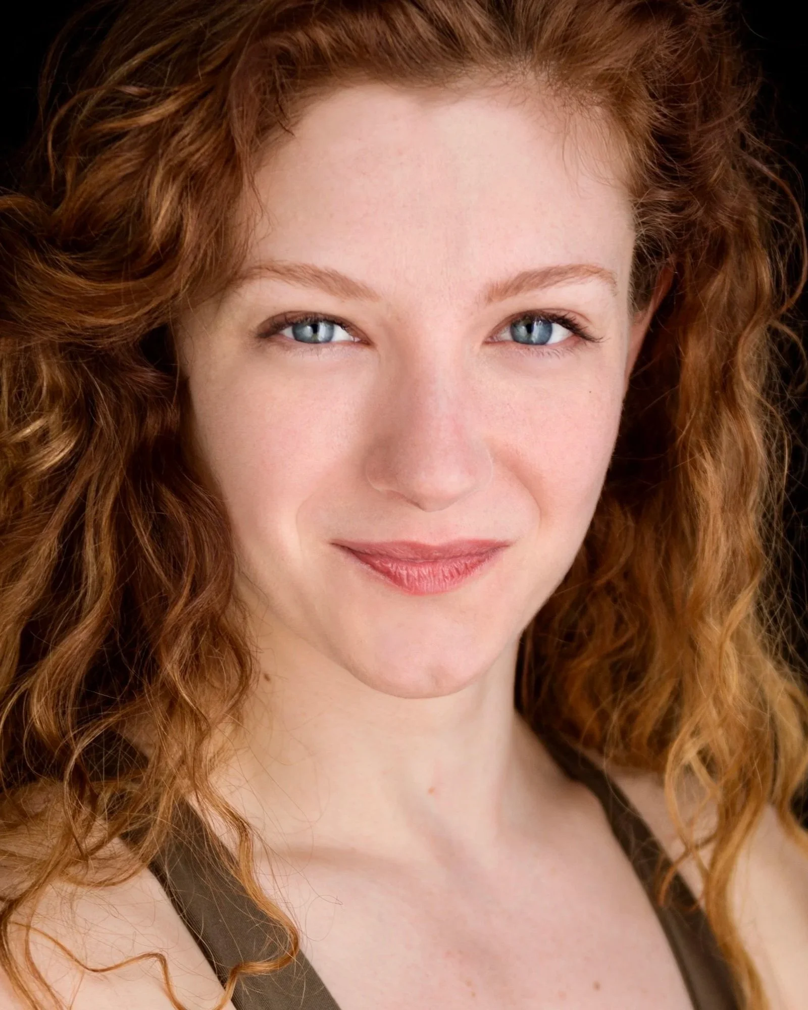 A close-up portrait of a woman with wavy red hair and blue eyes, smiling softly.