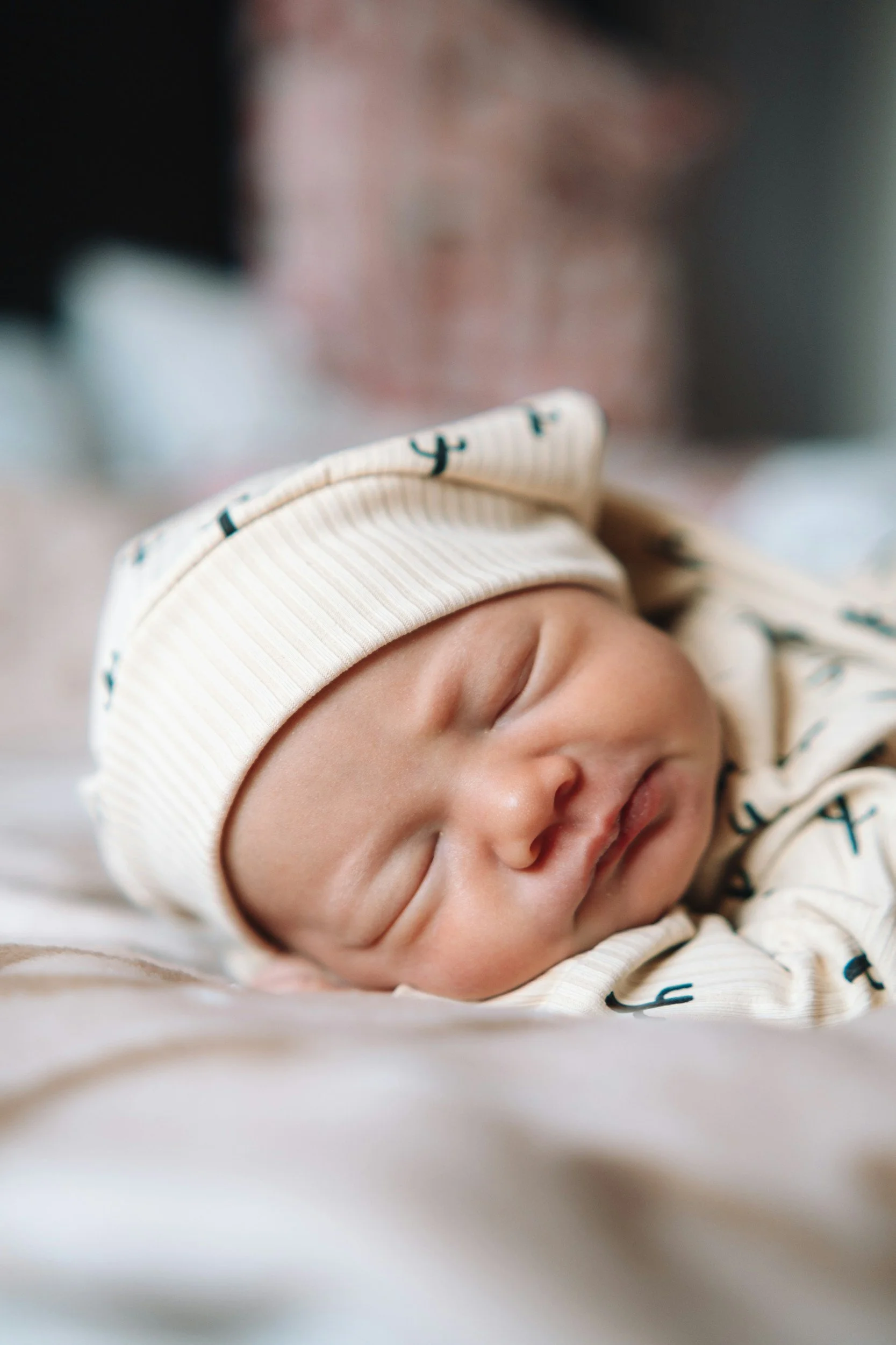 Close-up of a sleeping newborn baby wearing a striped hat and matching outfit with anchor patterns. He is resting after an infant massage session supporting baby comfort and bonding