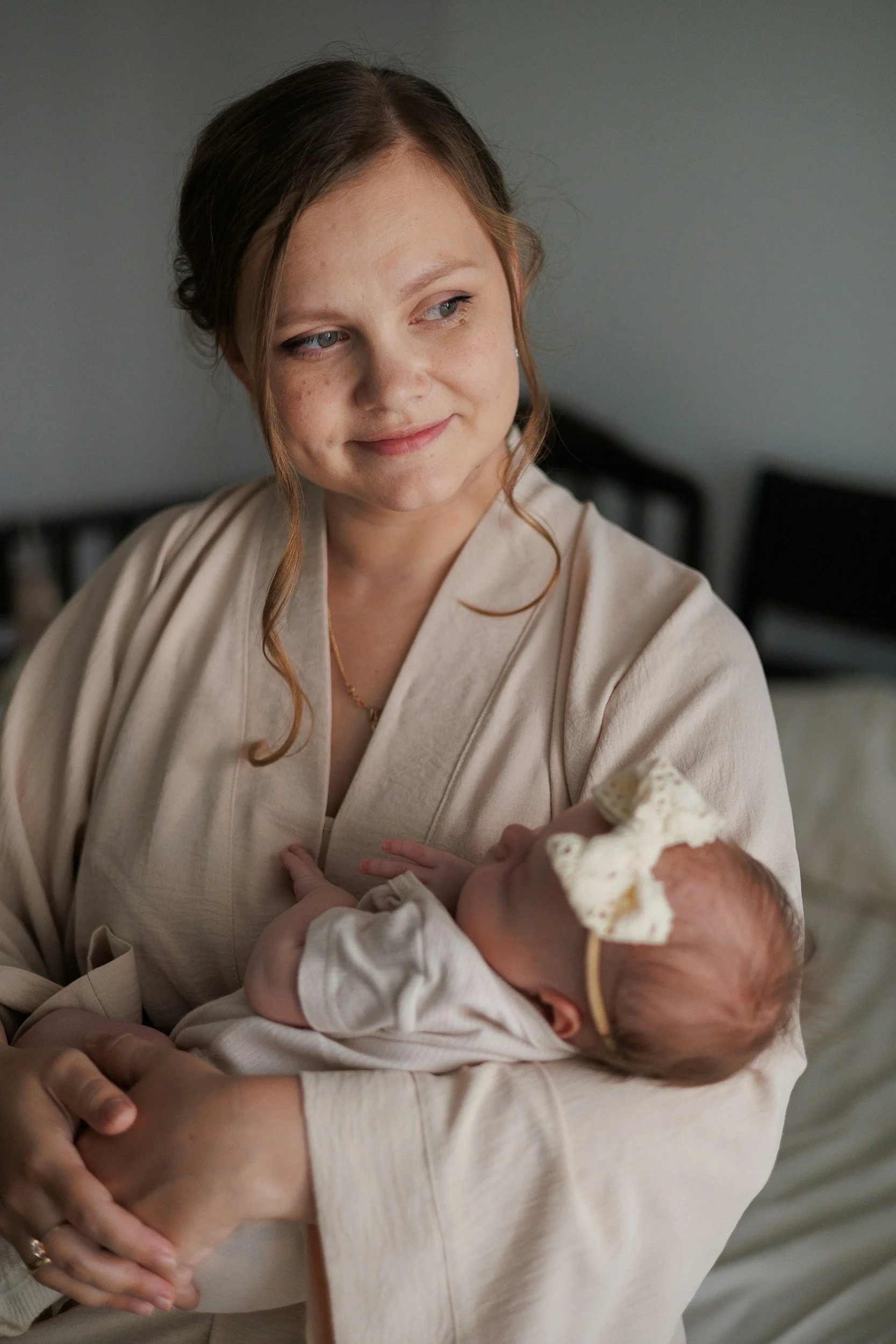 A woman holding a newborn baby in her arms, looking at the baby with a gentle smile. She is relieved to have received breastfeeding help for newborns and parents in Oregon