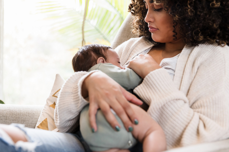 Woman in Madras Oregon, breastfeeding her baby while sitting on a couch during her in-home lactation consultation and after her therapeutic breast massage.
