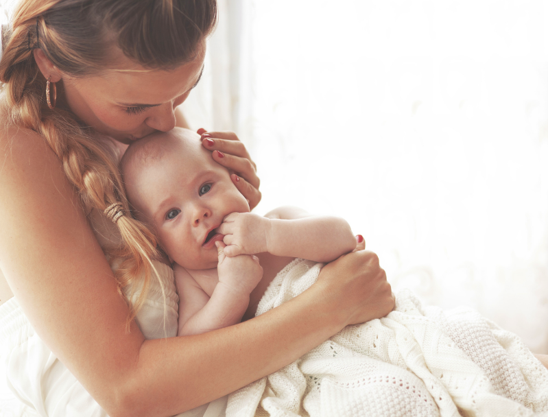 A woman holding a baby near a window with curtains, and gently holding baby in a peaceful, natural light environment in central Oregon