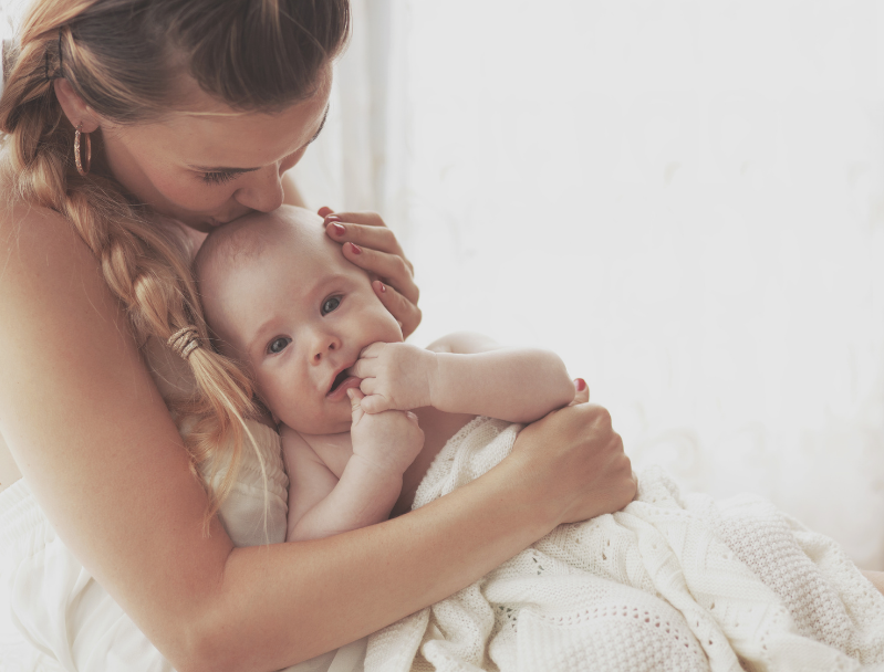 A woman with long blonde hair embraces her young baby, holding him close and kissing his forehead, after a successful breastfeeding session with Integrative Lactation Services