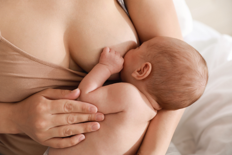 Close-up of a mother breastfeeding her infant, who is lying on her chest.