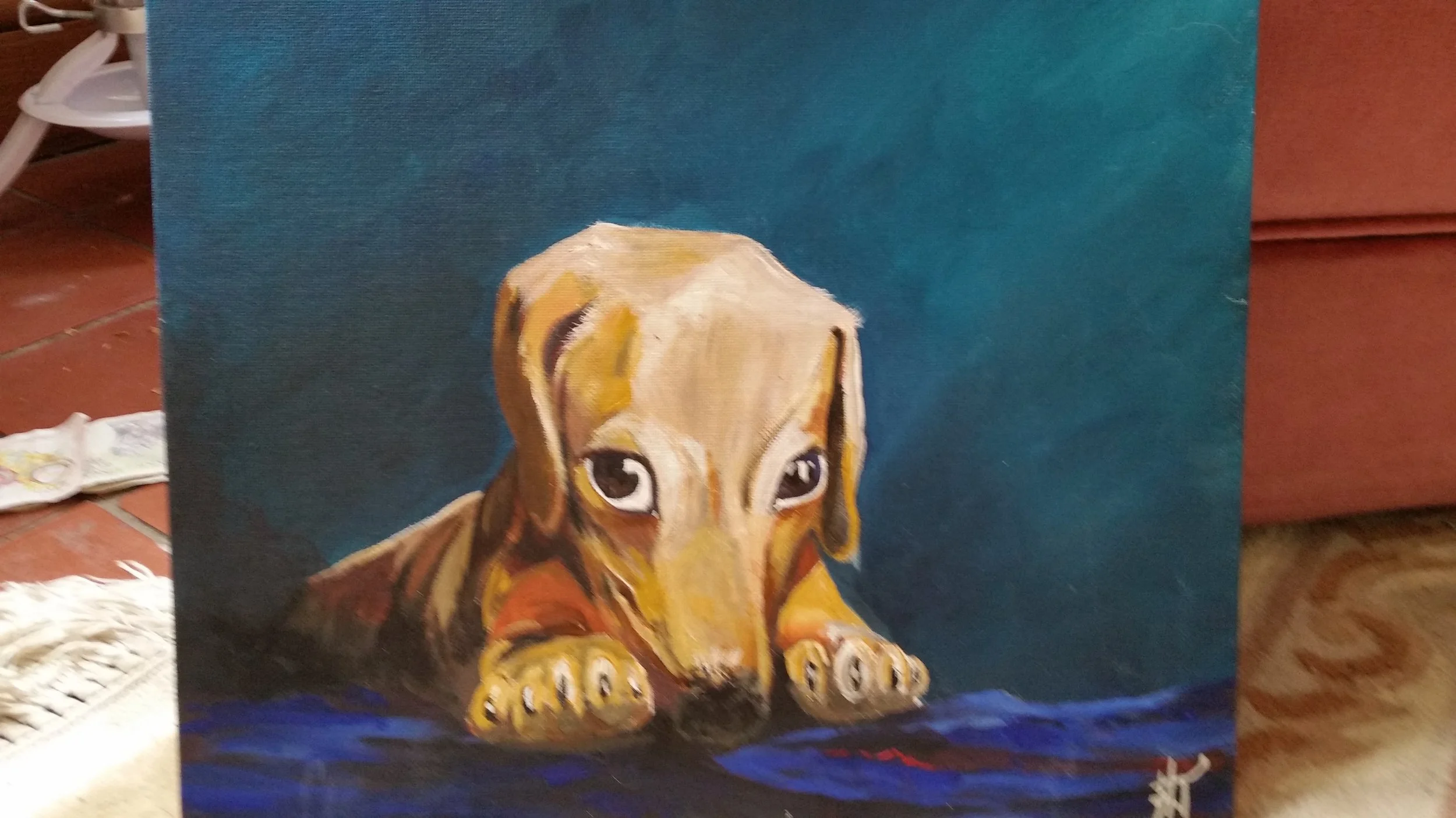 A painting of a cute brown and yellow puppy with big eyes lying down with its paws stretched out in front of it on a blue surface, with a solid dark teal background.