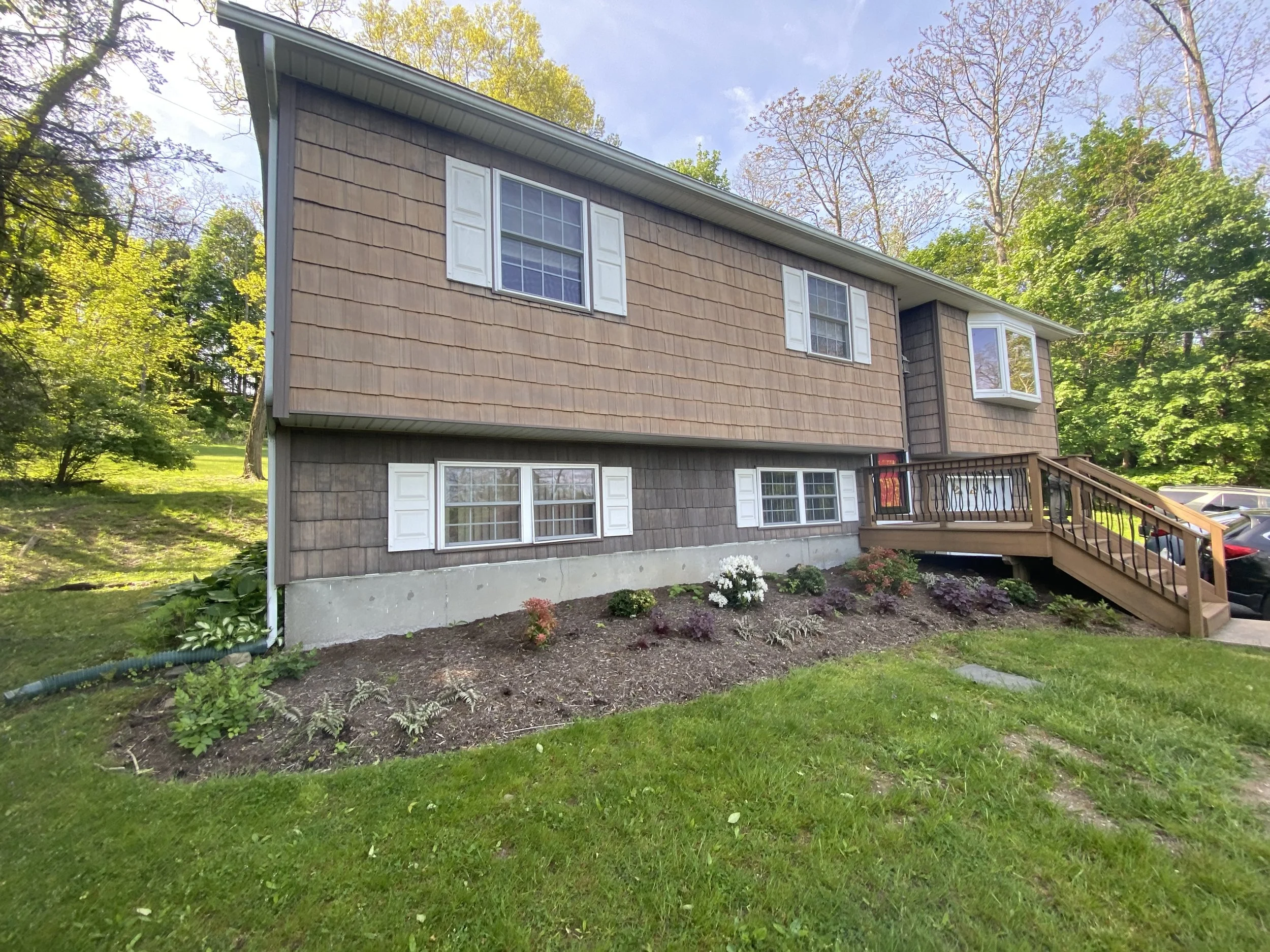Two-story suburban house with wooden siding, stairs, and garden