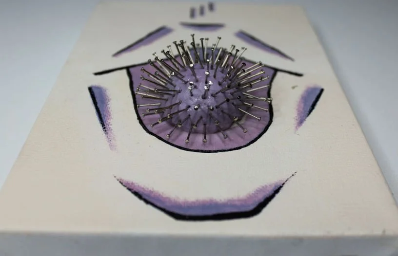 Title: Breast Feeding:

Breast Feeding is an abstracted mouth—open, exposed, and vulnerable. At its center, a foam ball stands in as the nipple, soft in form yet surrounded by protruding nails. The contrast between yielding and piercing materials ref