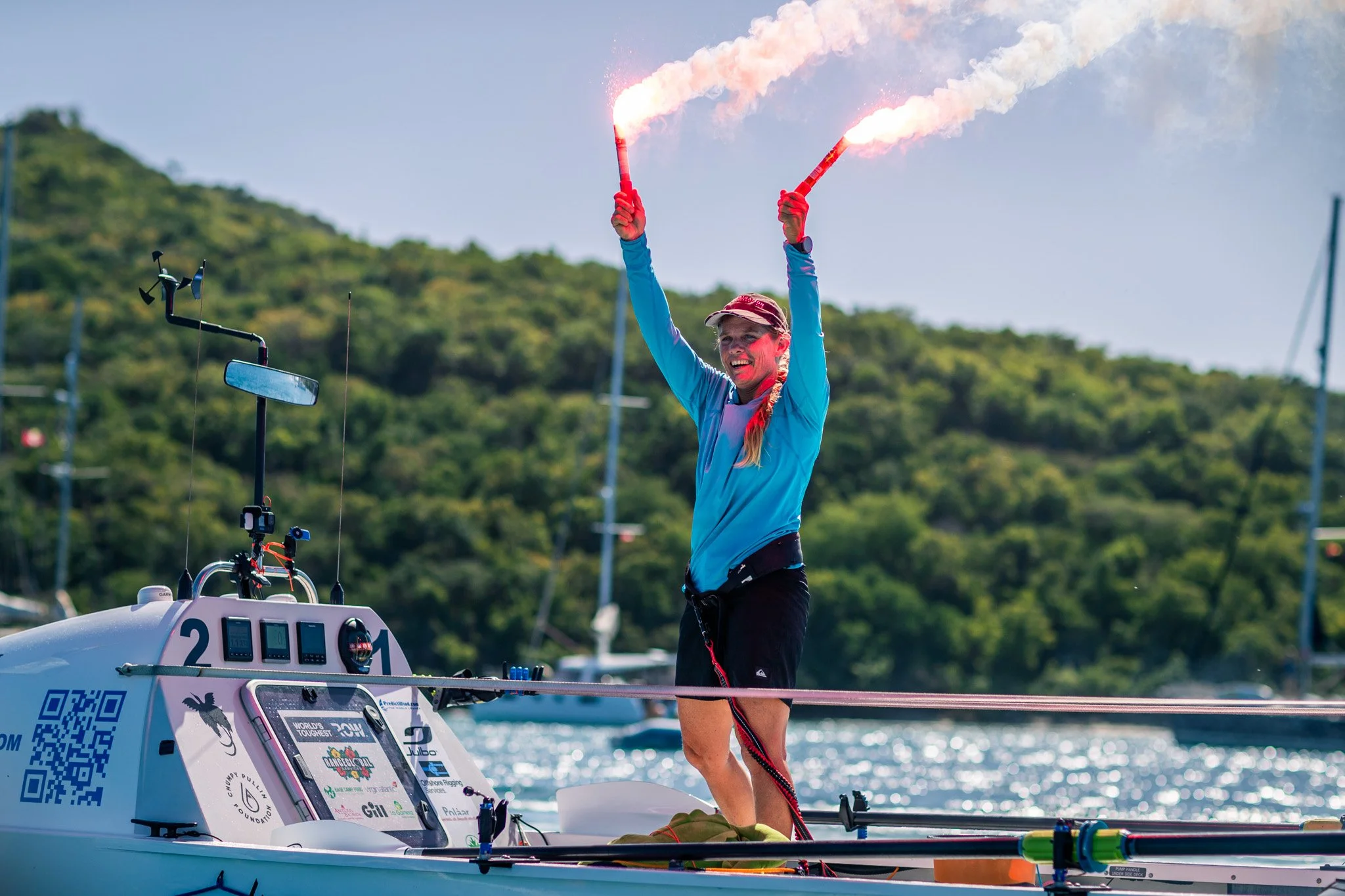 A woman in athletic clothing holding two flares emitting smoke on a boat during daytime.