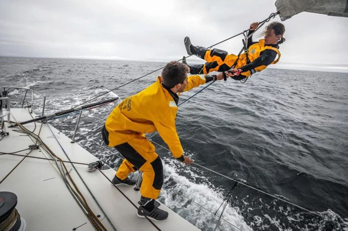 Liz Wardley working on the ropes over the side of an offshore racing yacht in rough seas.