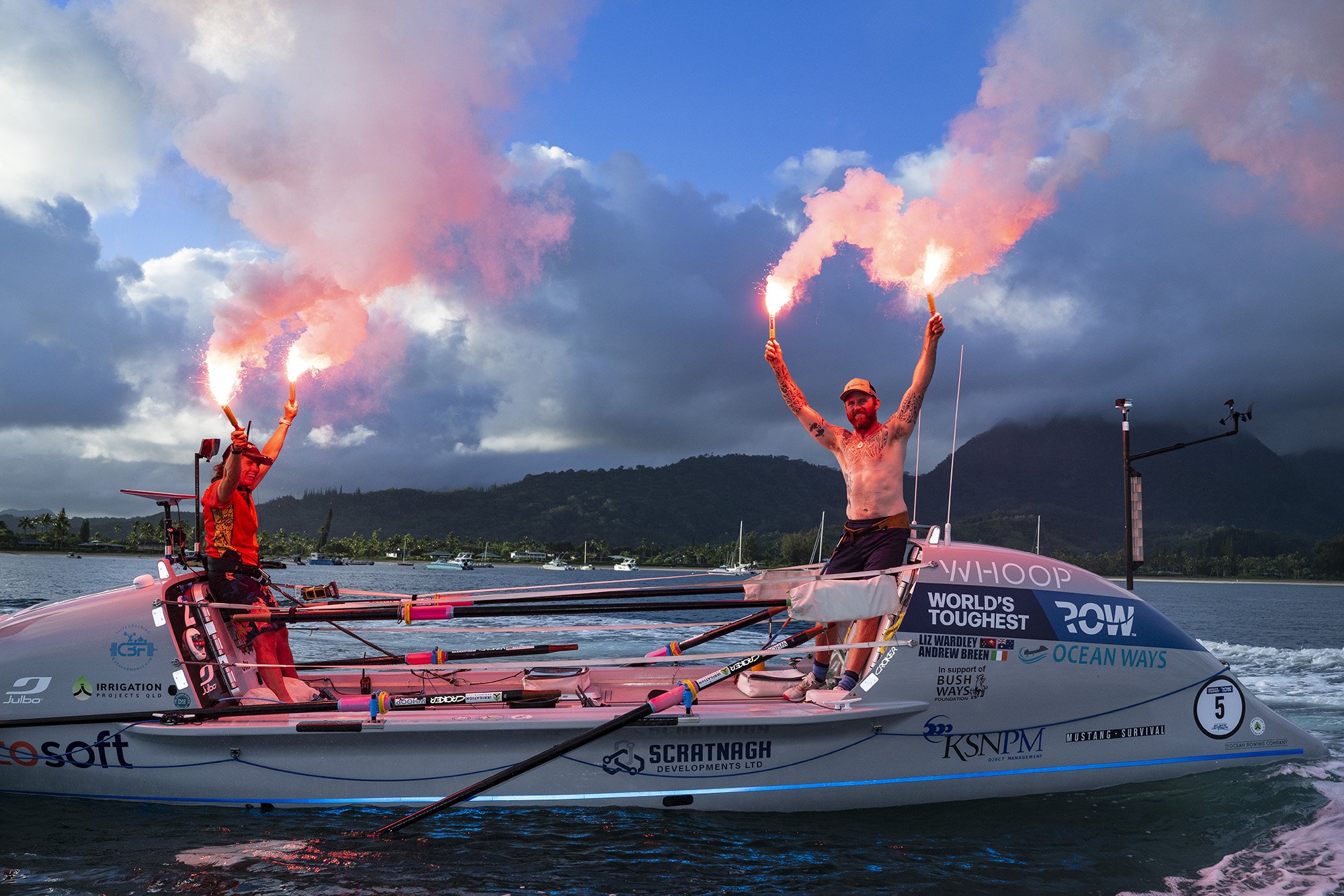 Two sailors on a boat, each holding flares emitting pink smoke, with a backdrop of mountains, clouds, and a choppy water scene.