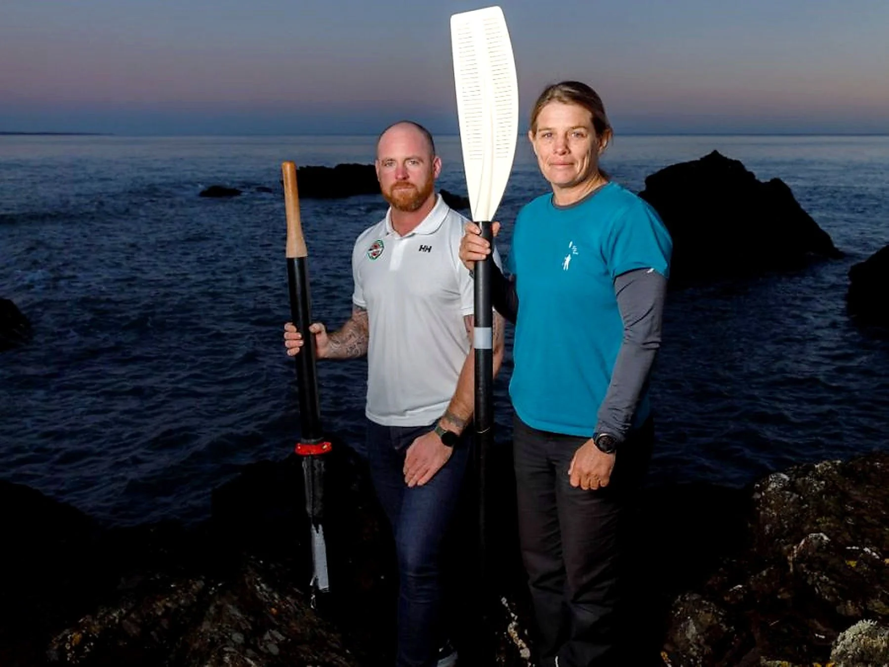 Liz Wardley and Andrew Breen holding oars beside the sea while preparing for their pairs ocean row across the Pacific.