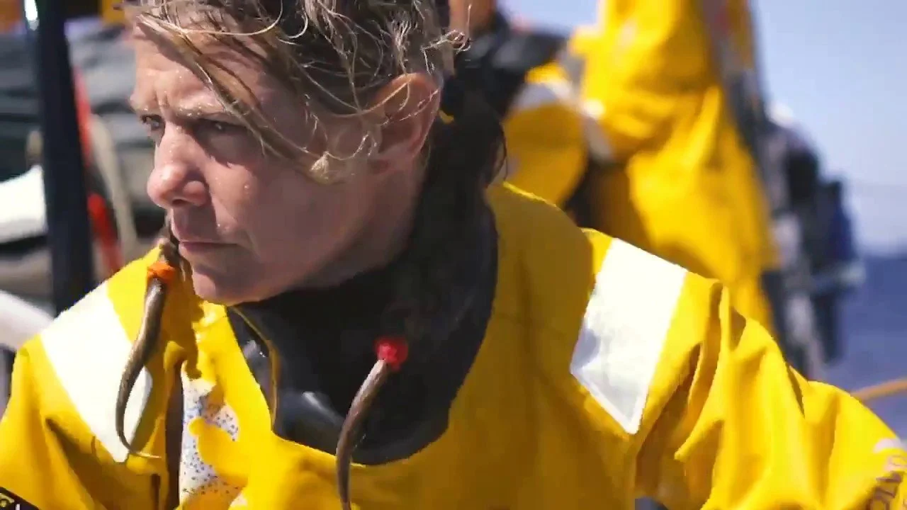 Close-up of Liz Wardley wearing yellow sailing waterproofs aboard a racing yacht.