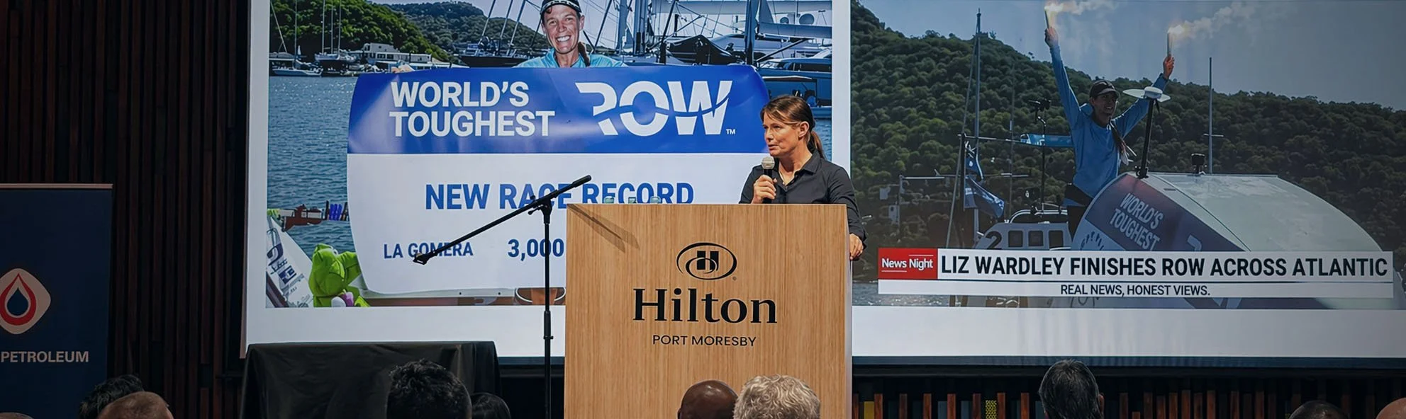 Liz Wardley speaking at a podium at Hilton Port Moresby talking about her solo ocean row as part of World's Toughest Row.