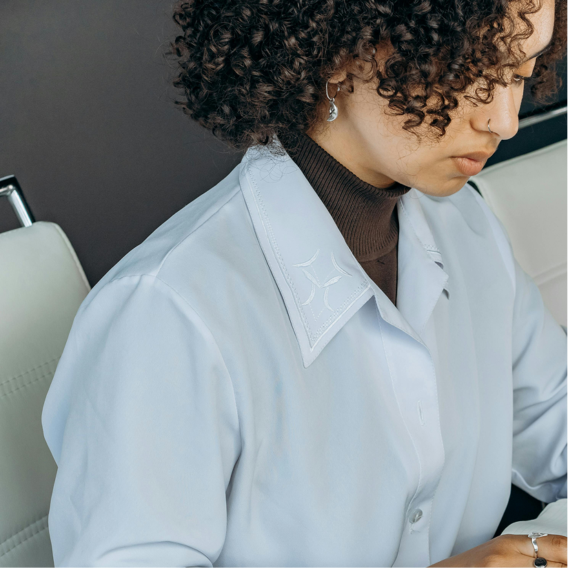 A woman with curly hair and earrings, dressed in a white lab coat, sitting in a professional setting.