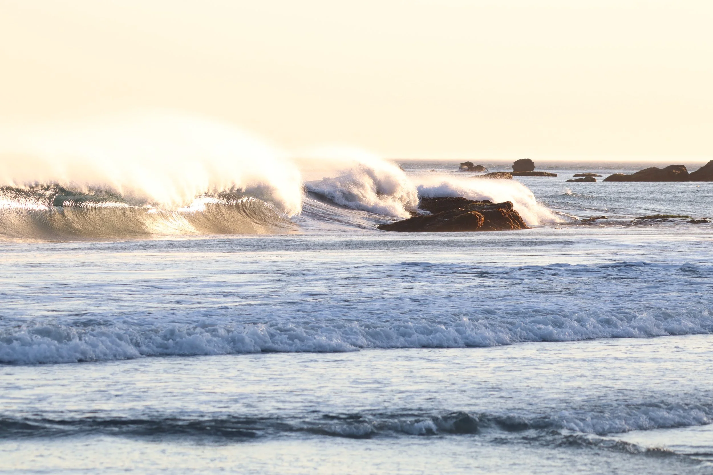 Waves crashing against rocks in the ocean during sunset.