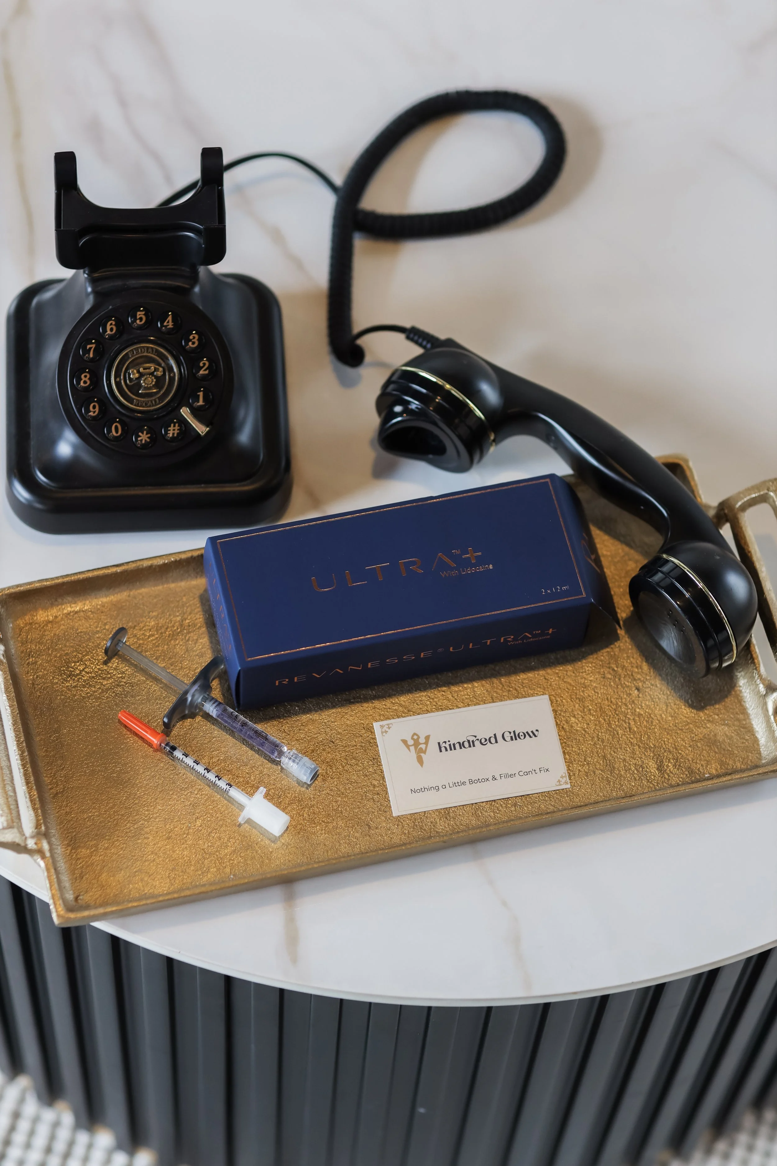 Vintage black rotary phone, medical syringes, and skincare product box on a gold tray