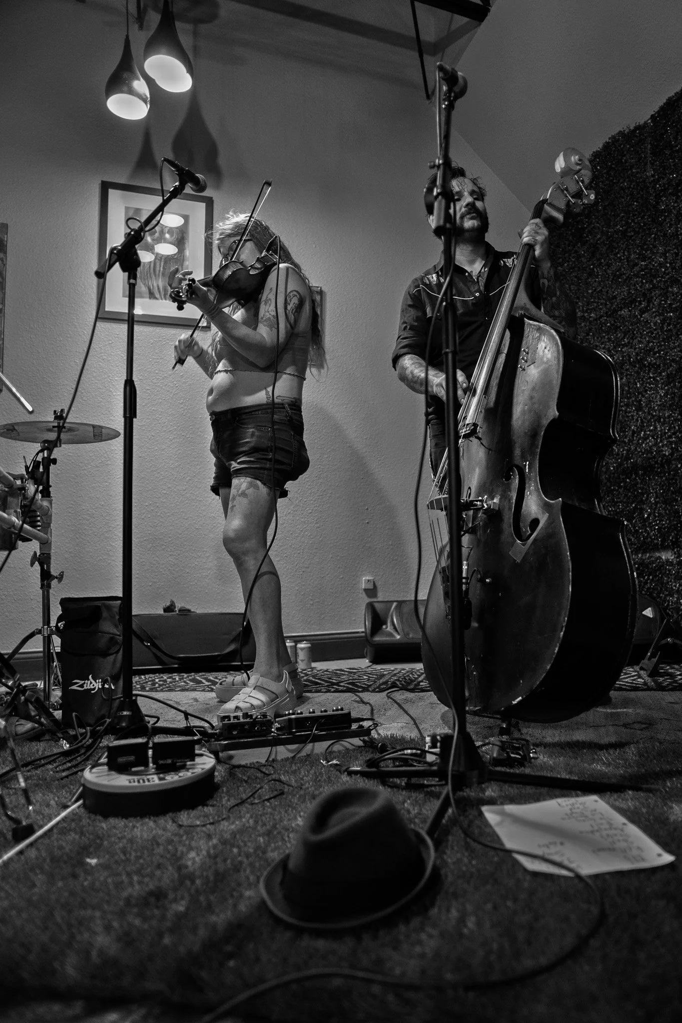A woman playing the violin and a man playing the double bass during a performance. The scene takes place indoors with music equipment and microphones visible.