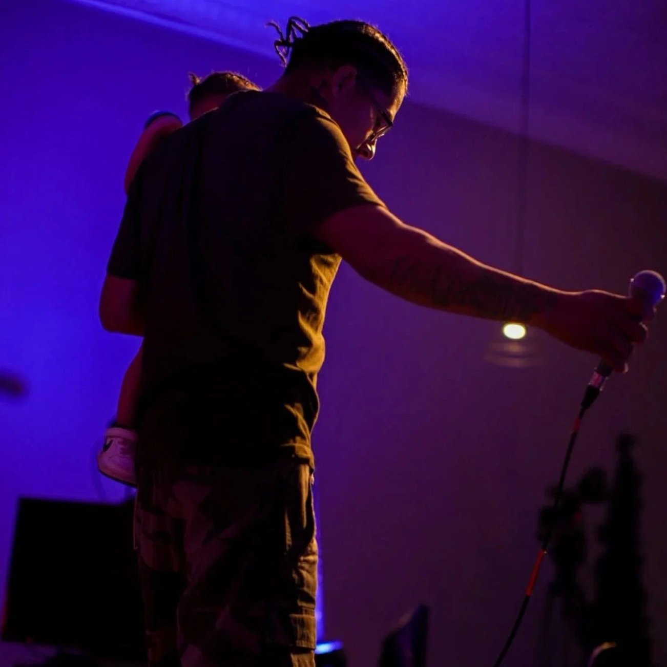 Person holding a microphone on stage with purple and blue lighting, silhouette style.