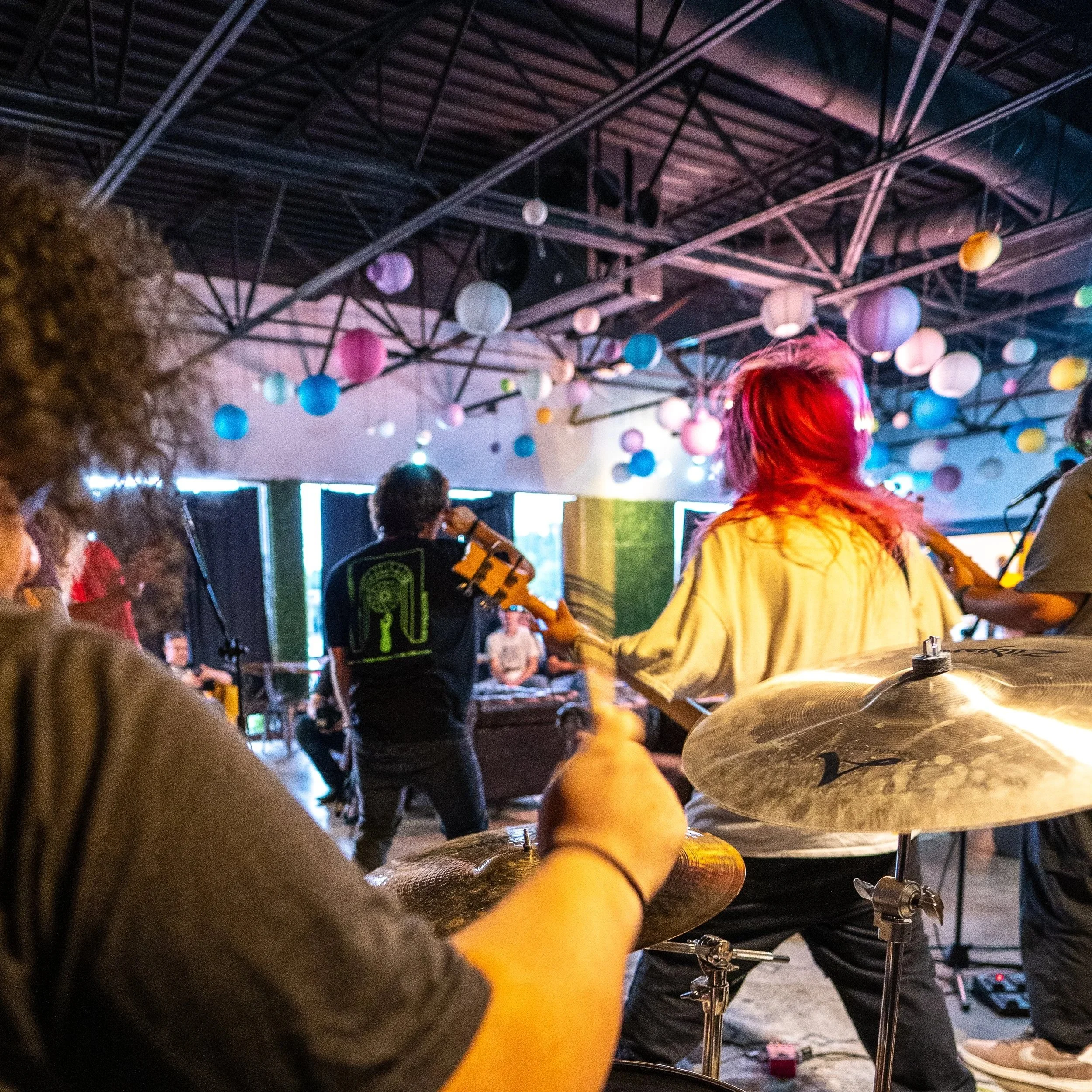 People playing drums at an indoor event decorated with colorful paper lanterns hanging from the ceiling.