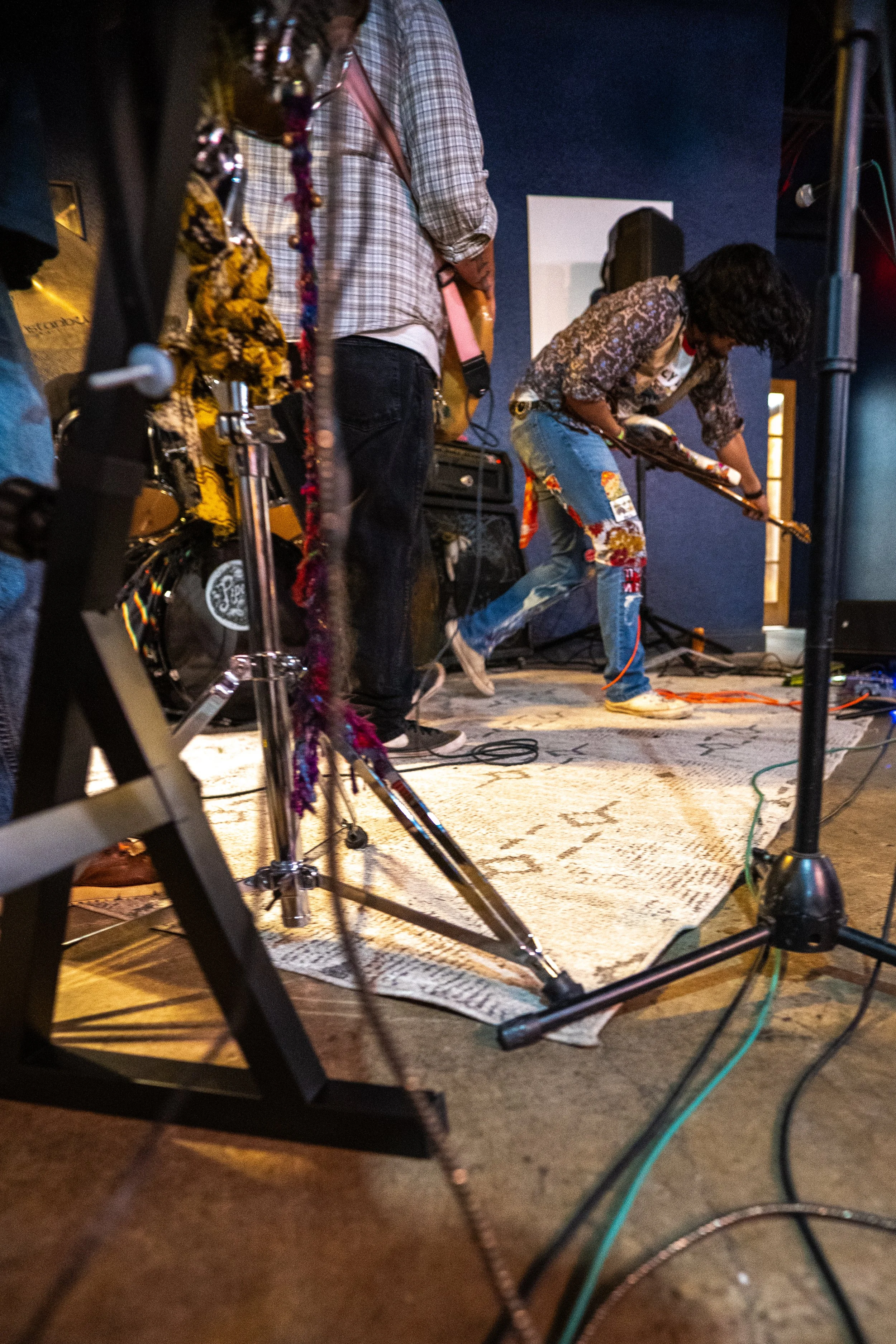 People performing music on stage, playing guitars and singing, with microphones and stage equipment around.
