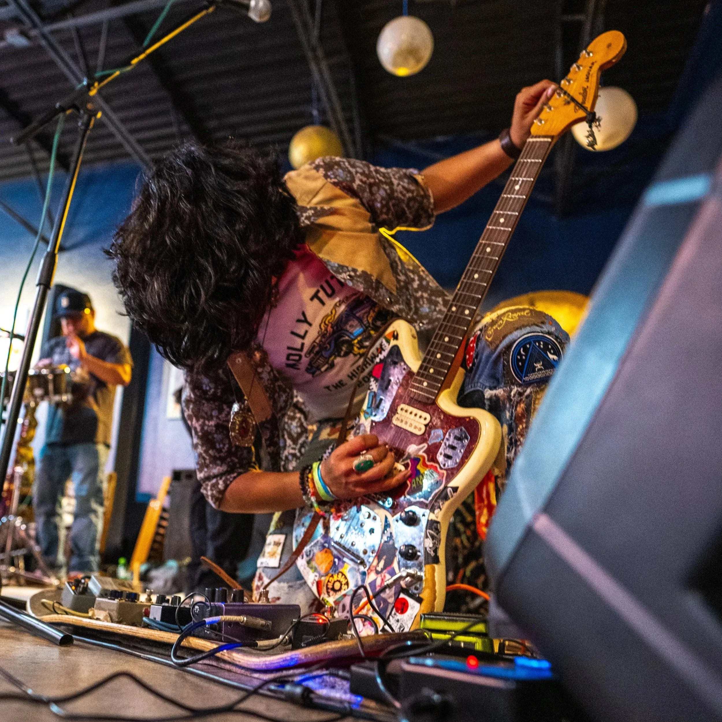 A musician playing an electric guitar at a music event with various equipment and cables on the ground.
