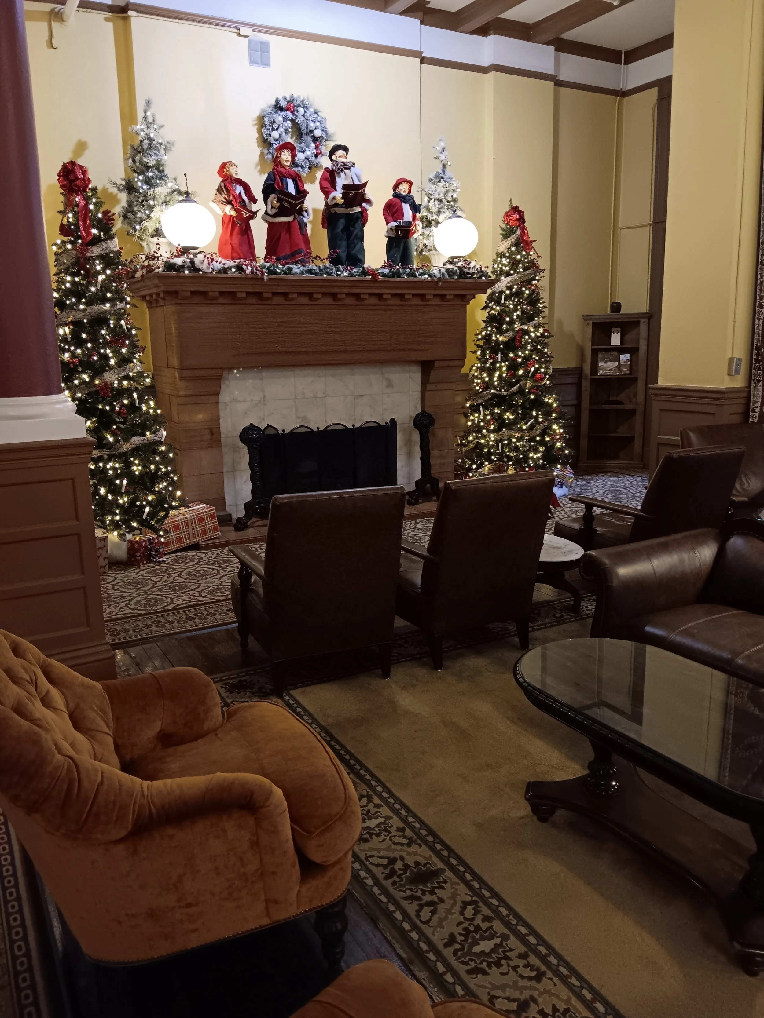 Festively decorated living room with a fireplace, Christmas trees, and holiday figurines on the mantel.