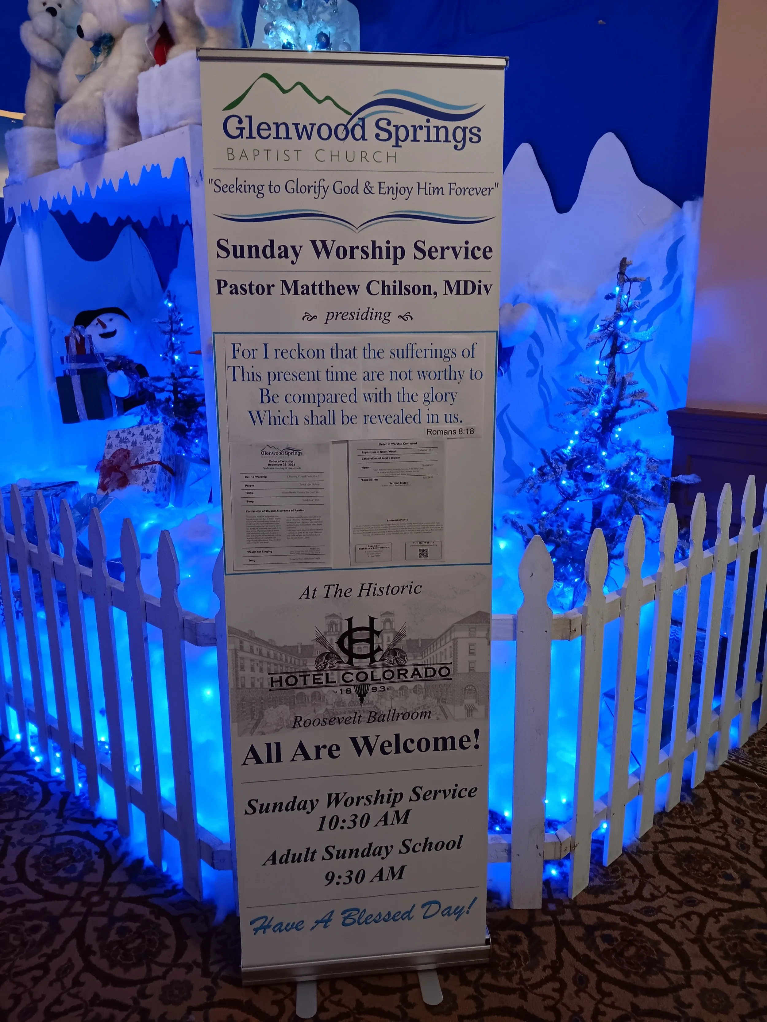 Sign promoting Sunday worship services at Glenwood Springs Baptist Church, held at the Hotel Colorado Roosevelt Ballroom. Includes timings for church service at 10:30 AM and adult Sunday school at 9:30 AM, with festive decorations and Christmas-theme