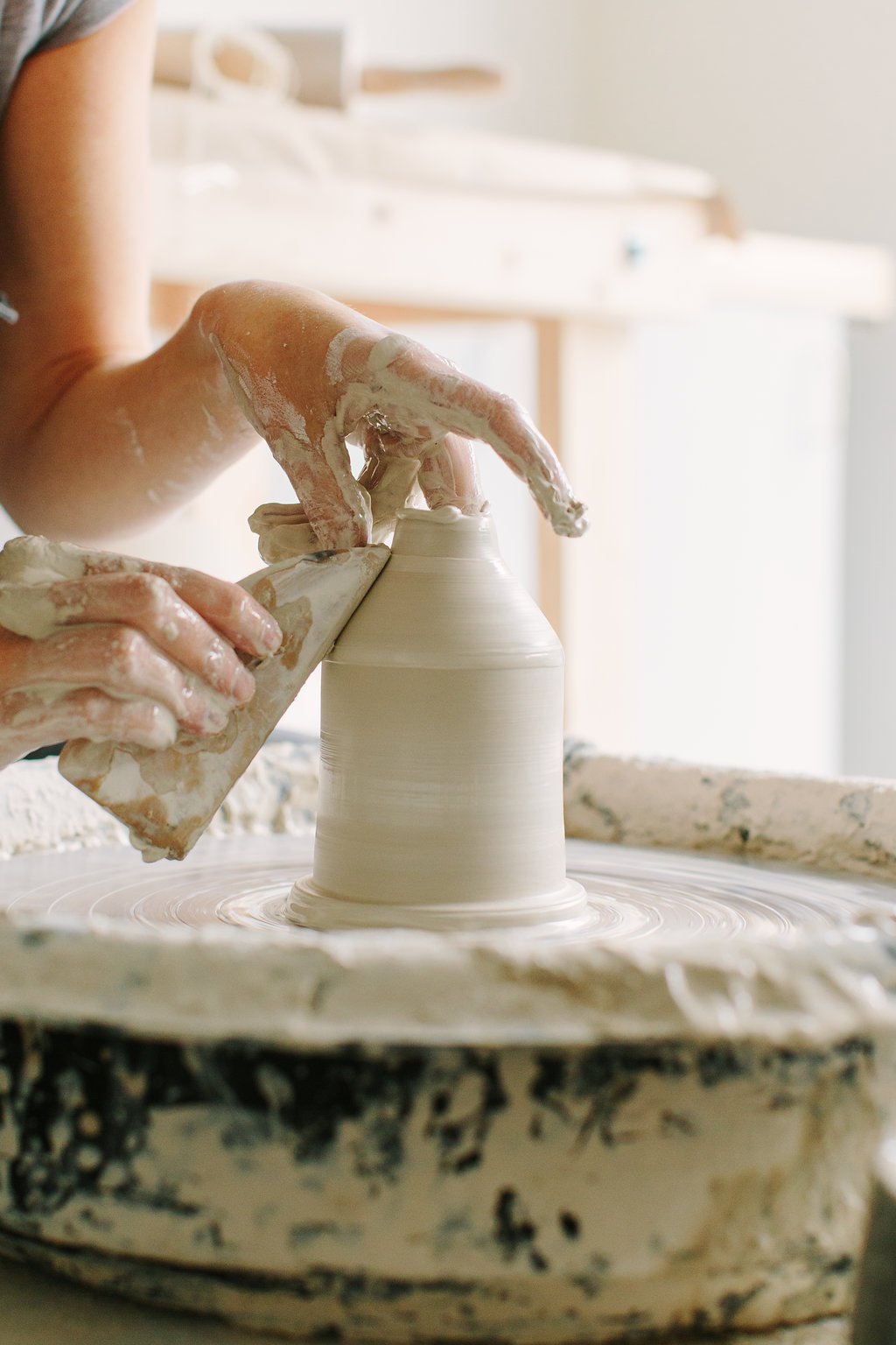 Close-up of a person shaping a ceramic vase on a pottery wheel, hands covered in wet clay.