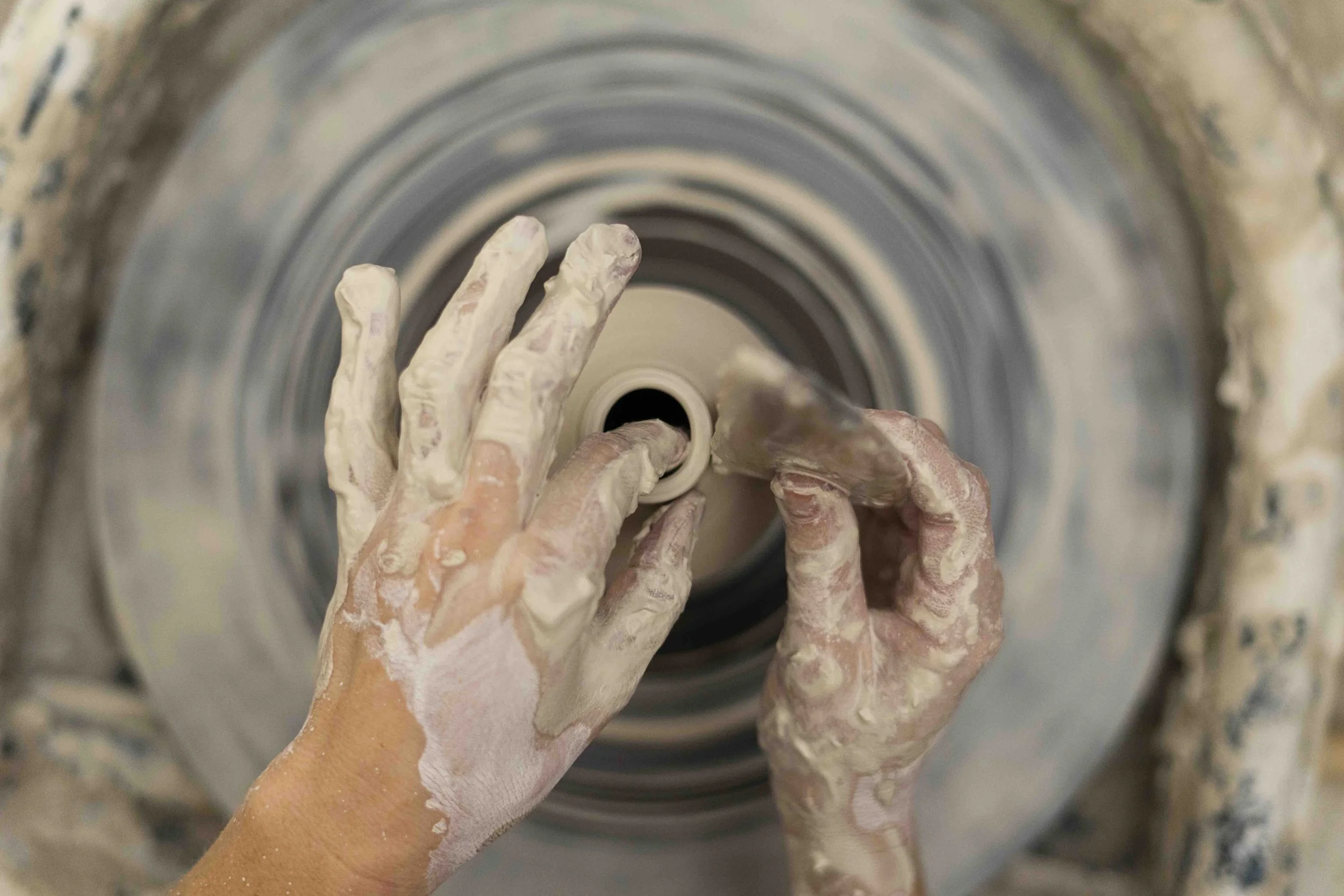 Hands covered in clay working on a pottery wheel creating a ceramic piece.