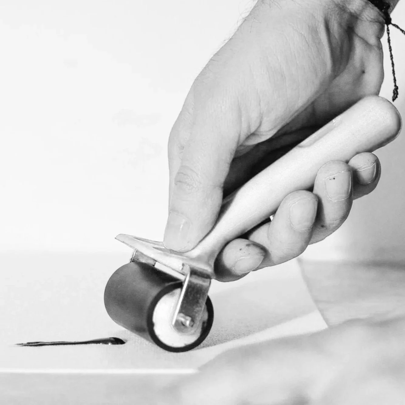 Black and white photograph of a hand using a roller to flatten paper.