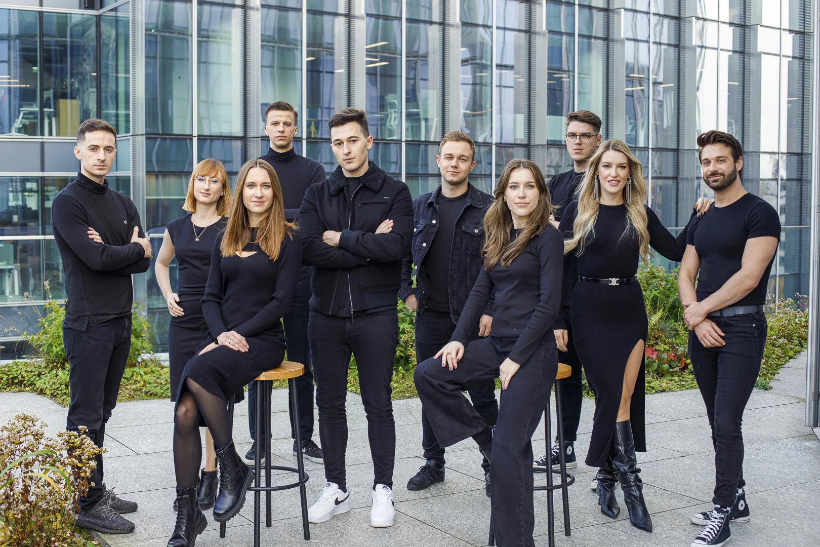 A group of ten people, dressed in black, posing outdoors on a balcony with modern glass buildings in the background.