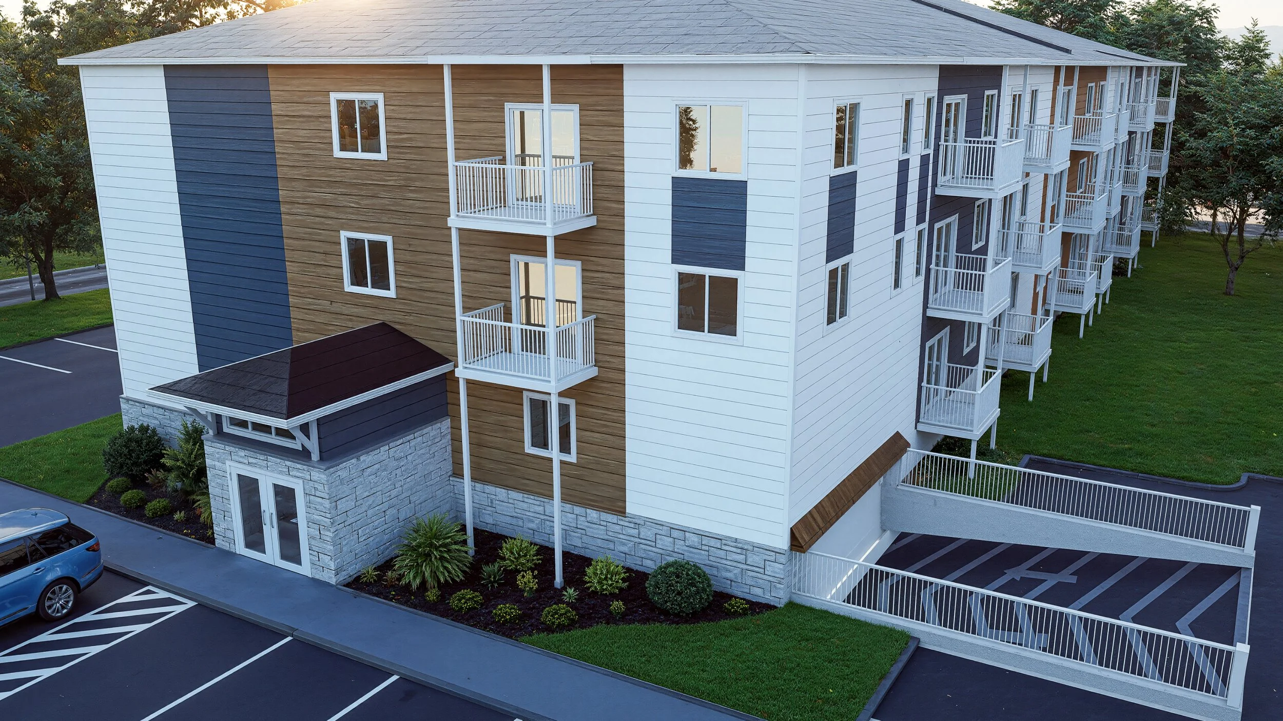 A multi-story apartment building with white, blue, and wood-paneled exterior walls, multiple balconies, and a parking area with several marked spaces.