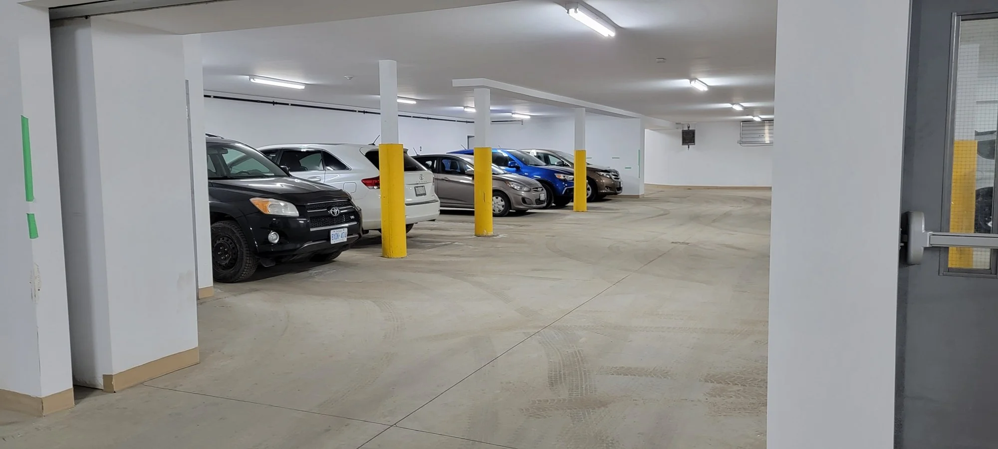 Underground parking garage with several parked cars, white walls, and fluorescent lighting.