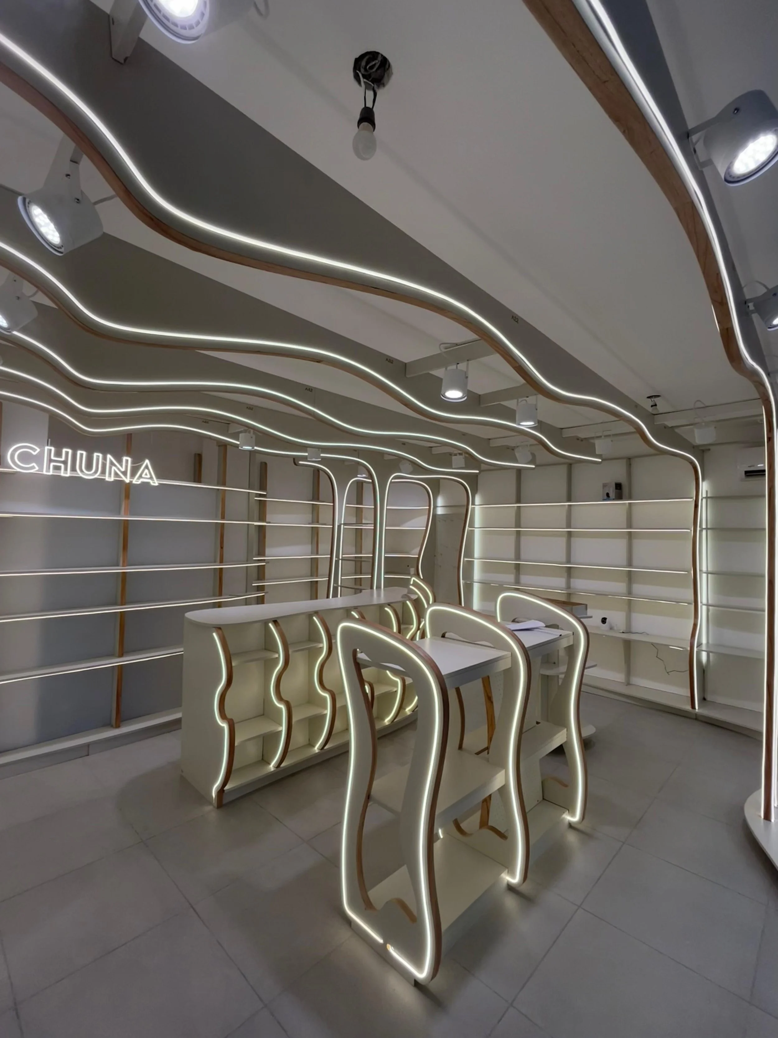 Interior moderno con mobiliario blanco y luces LED, incluyendo estantes y mesas, en un espacio de diseño futurista.