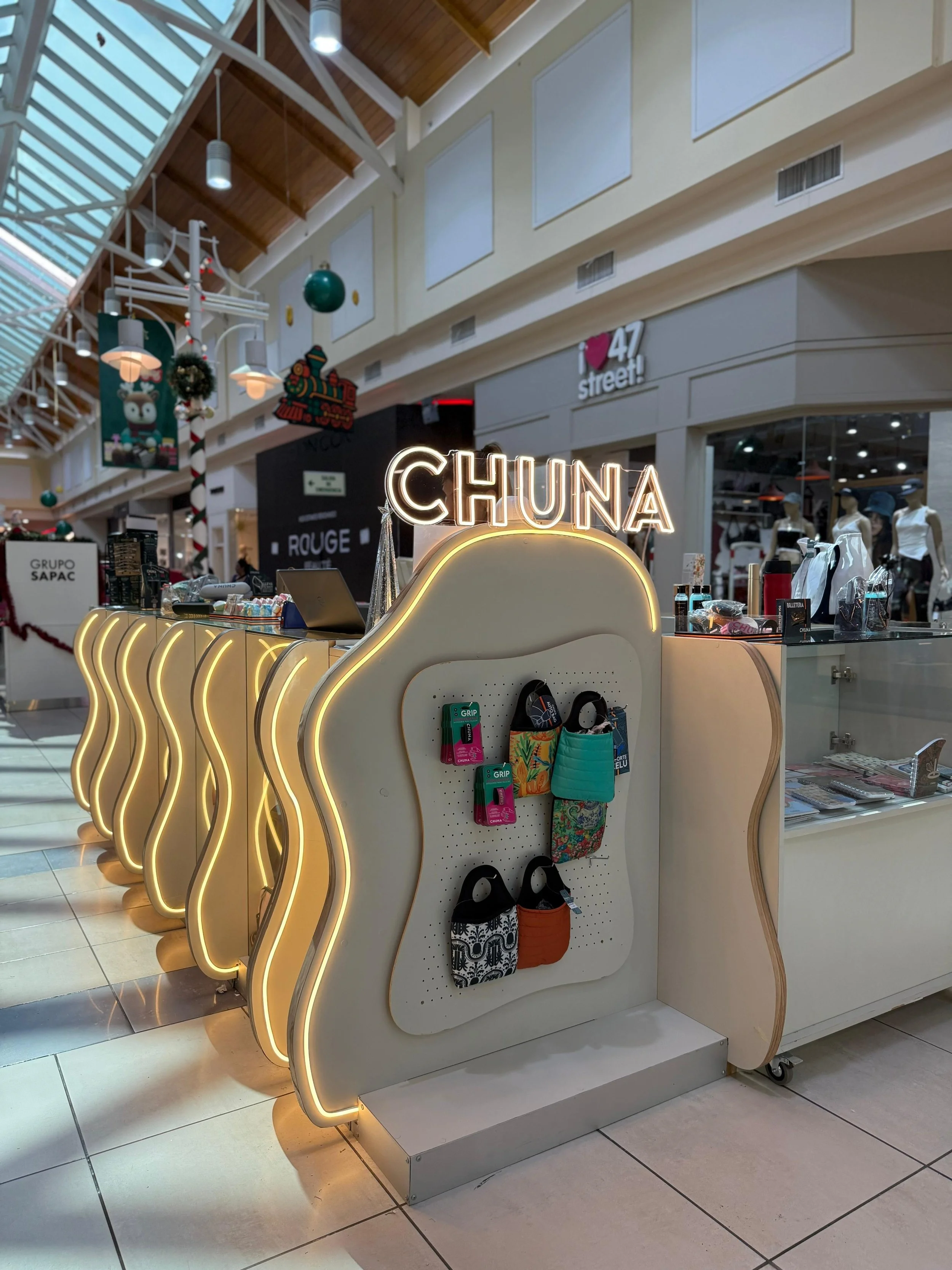 Mostrador de venta llamado 'CHUNA' en un centro comercial, con decoración de luces y artículos de accesorios en exhibición, en un ambiente festivo con decoraciones navideñas.