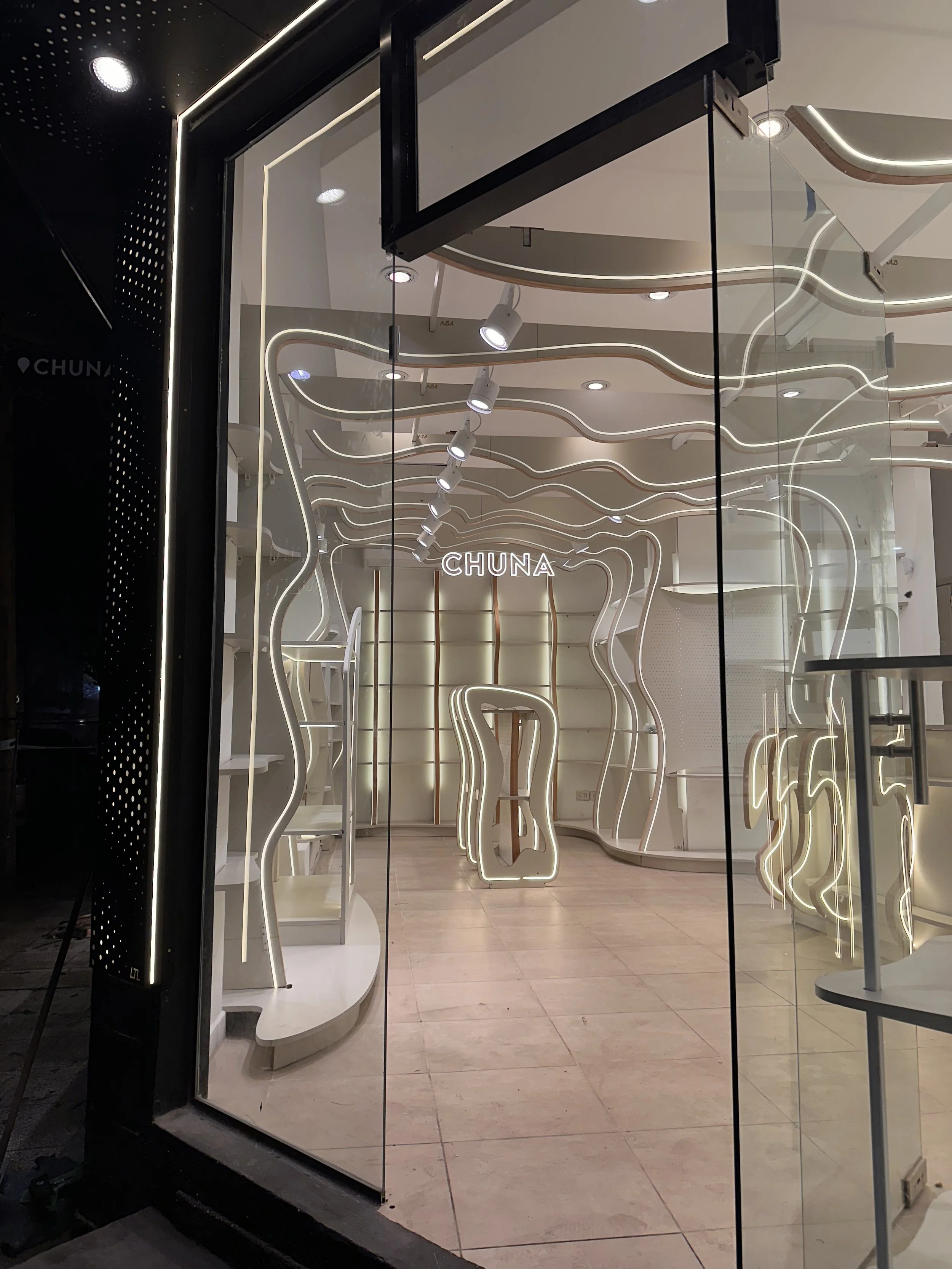 Vista de una tienda con decoración moderna, iluminación de neón y el nombre 'CHUNA' en la pared del fondo.