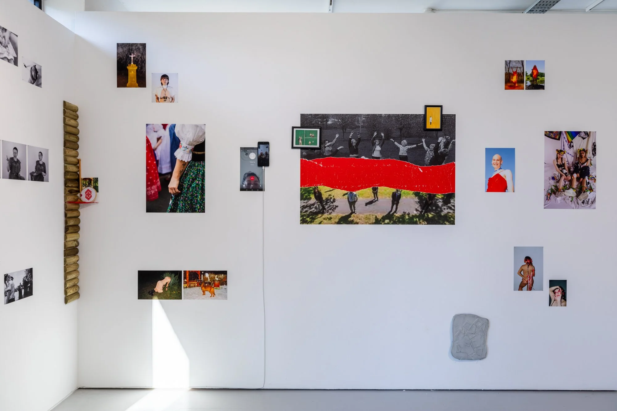 Gallery wall with various photographs and artworks, including black and white, color, and mixed media images, arranged on a white wall.