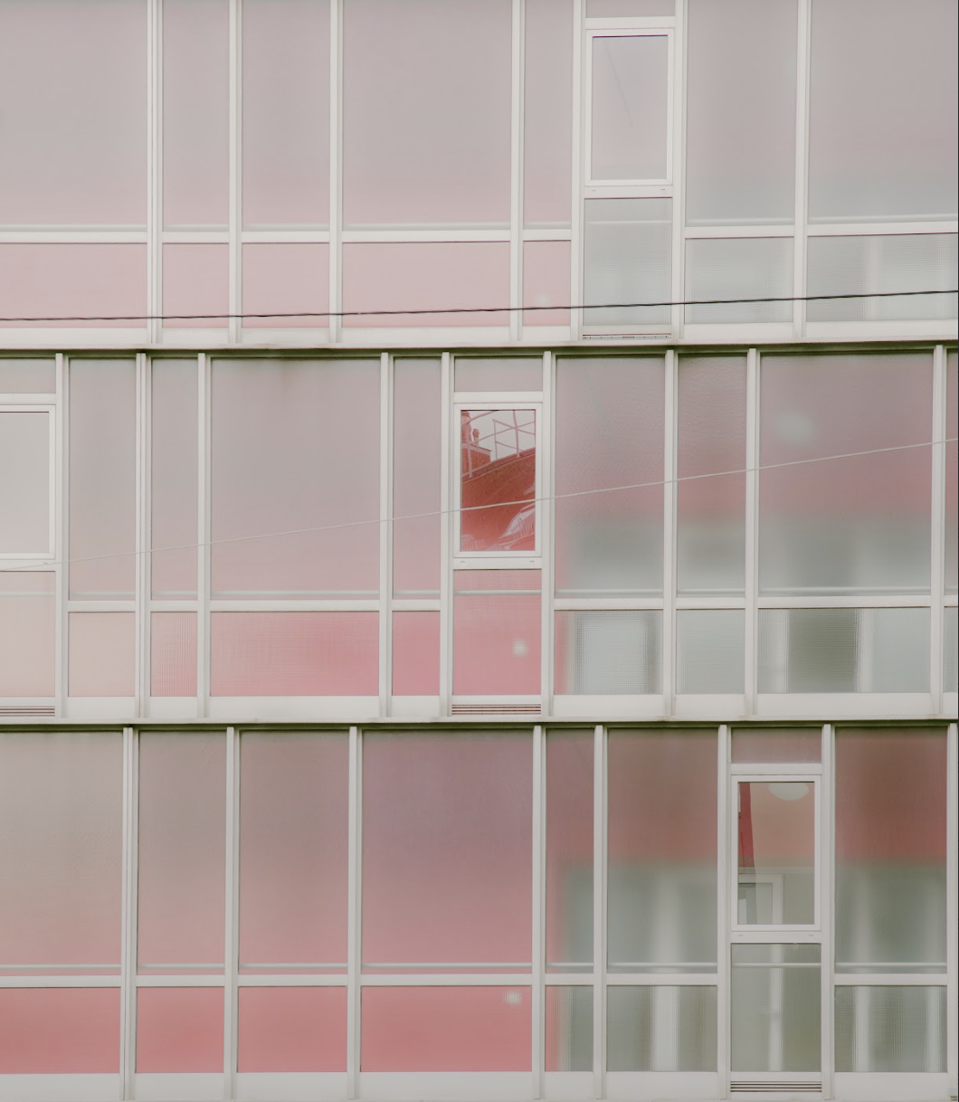 Close-up of a multi-story building's glass facade with pink and frosted panels and windows, some with reflections and partially open doors.