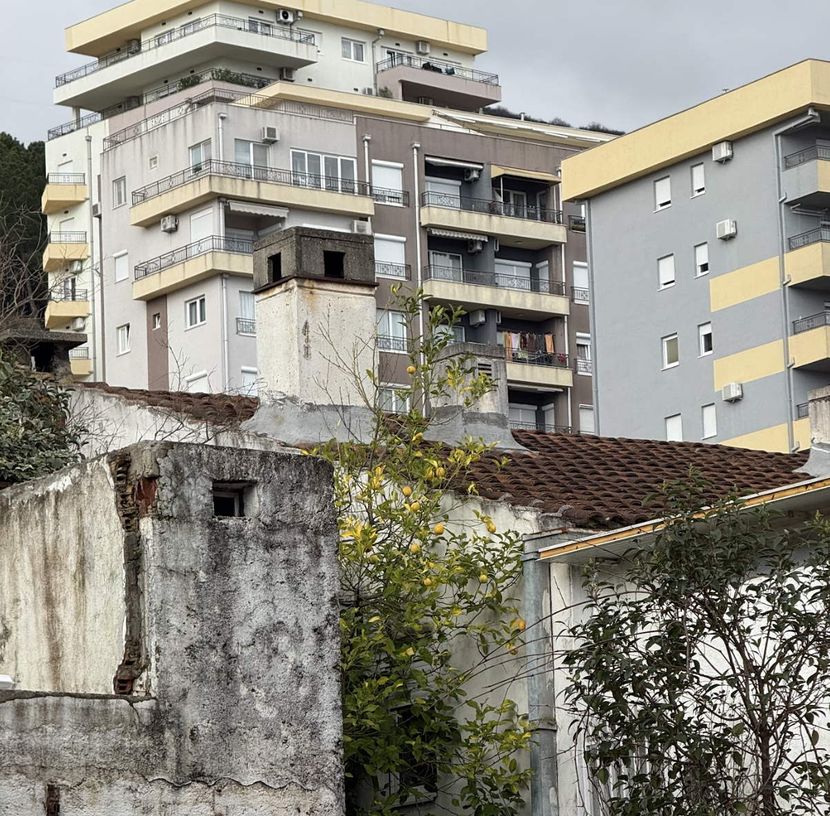 Contrast between old, weathered house wall with chimneys and modern high-rise apartments in the background.