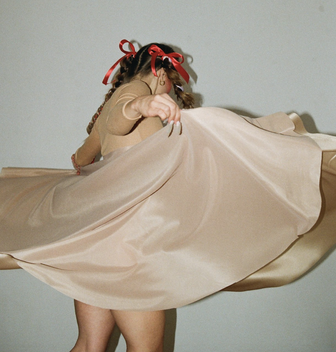 Woman with braided hair and red ribbons lifting beige satin fabric.