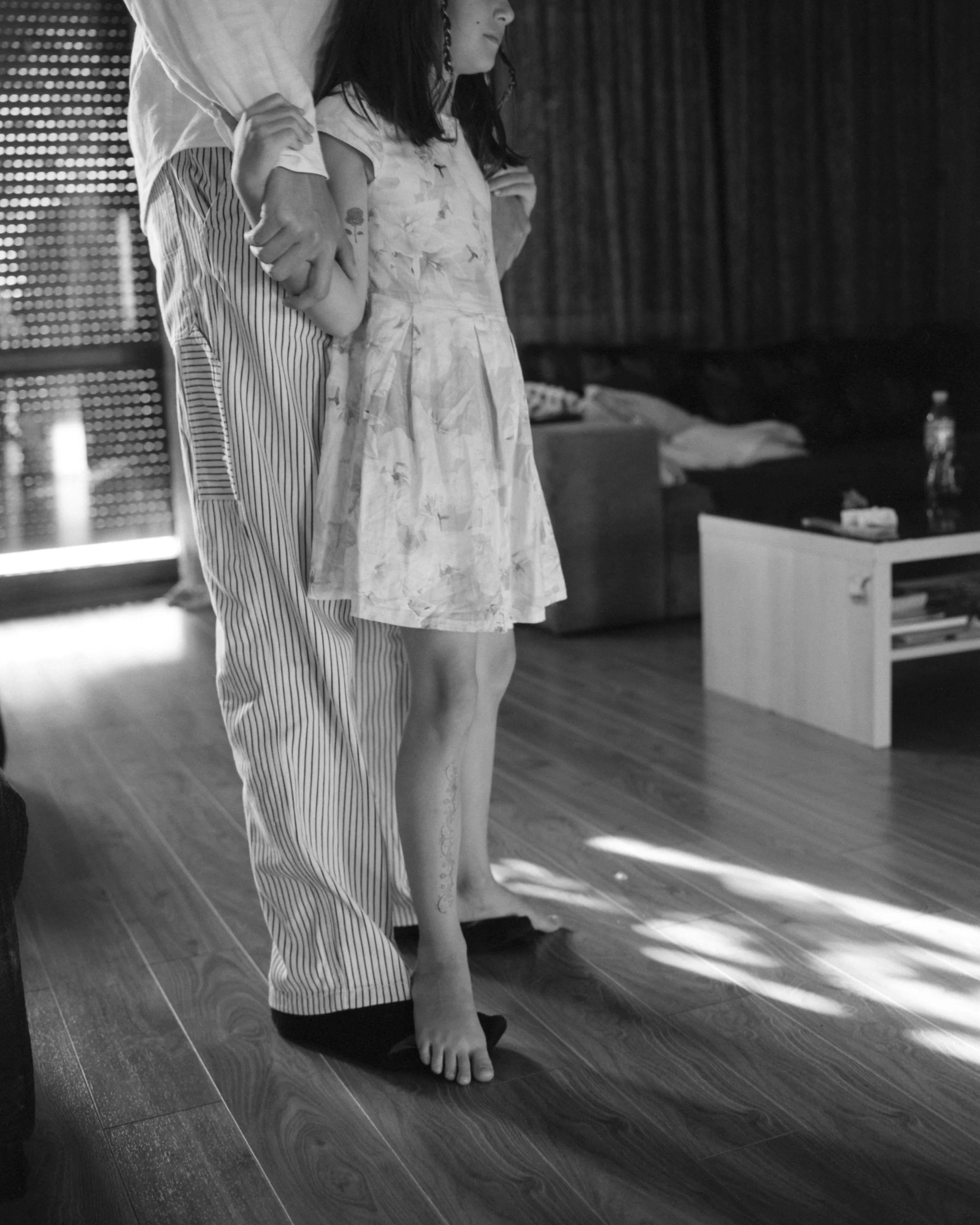 A child standing on the floor with an adult behind them holding their arm.