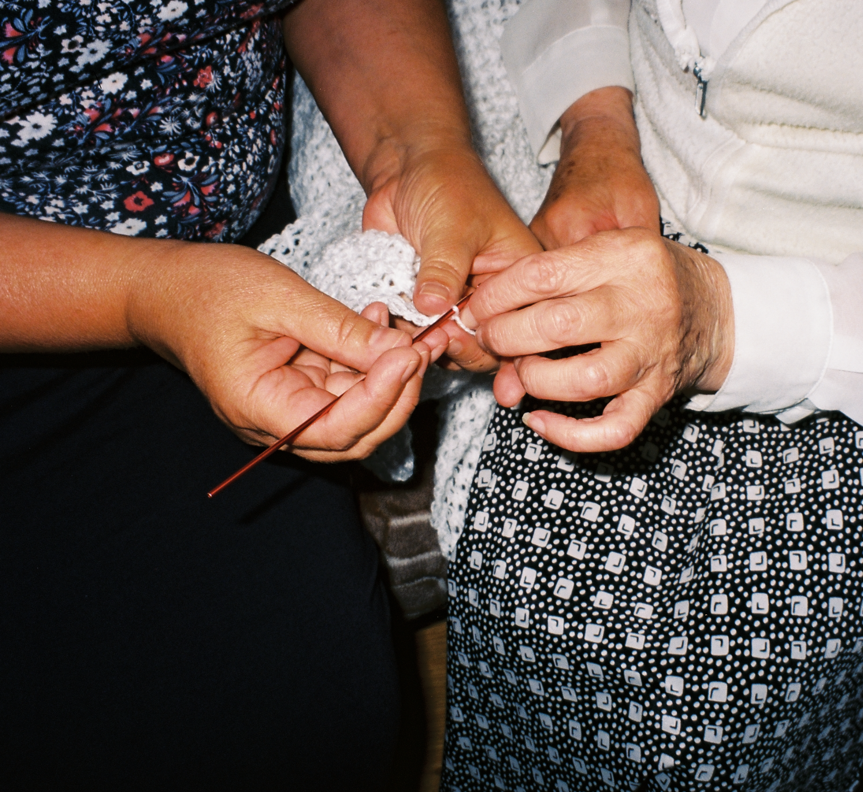 Close-up of two people sewing a white piece of fabric together with a needle and thread.