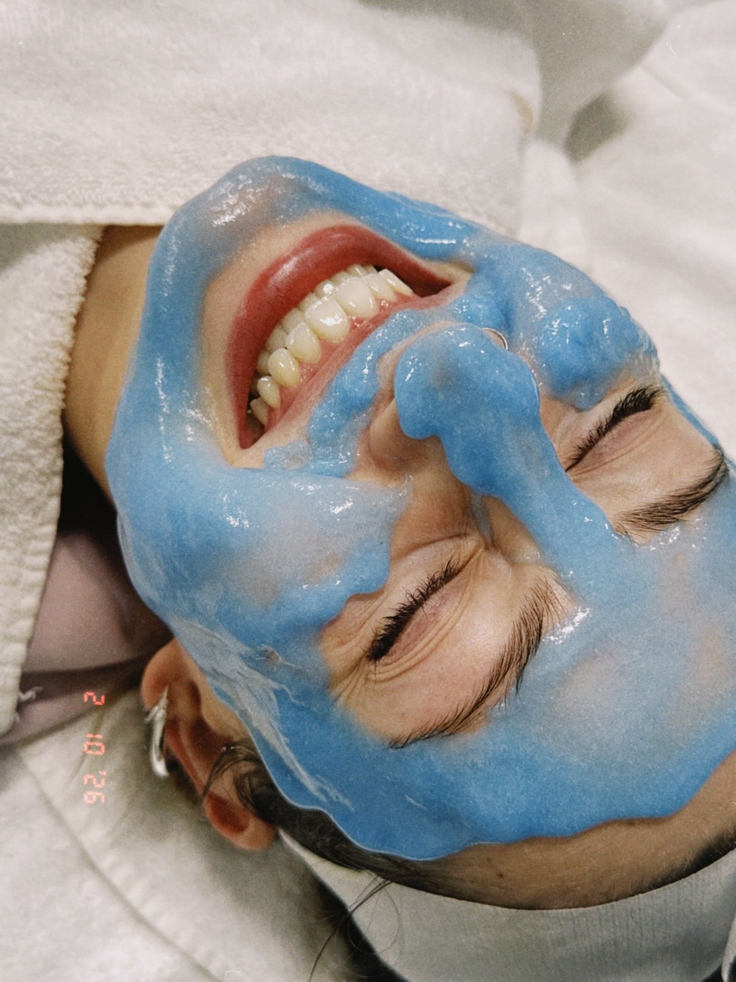 Person receiving a facial treatment with a blue mask applied to their face, lying down with eyes closed.