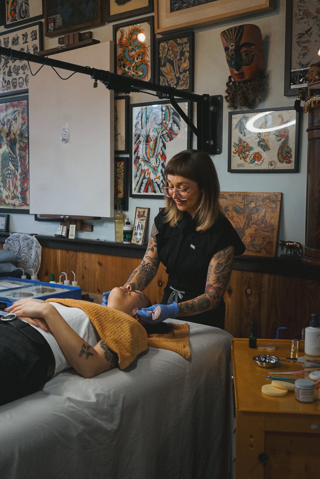 Esthetician performing a facial on a client in a studio decorated with artwork and masks.