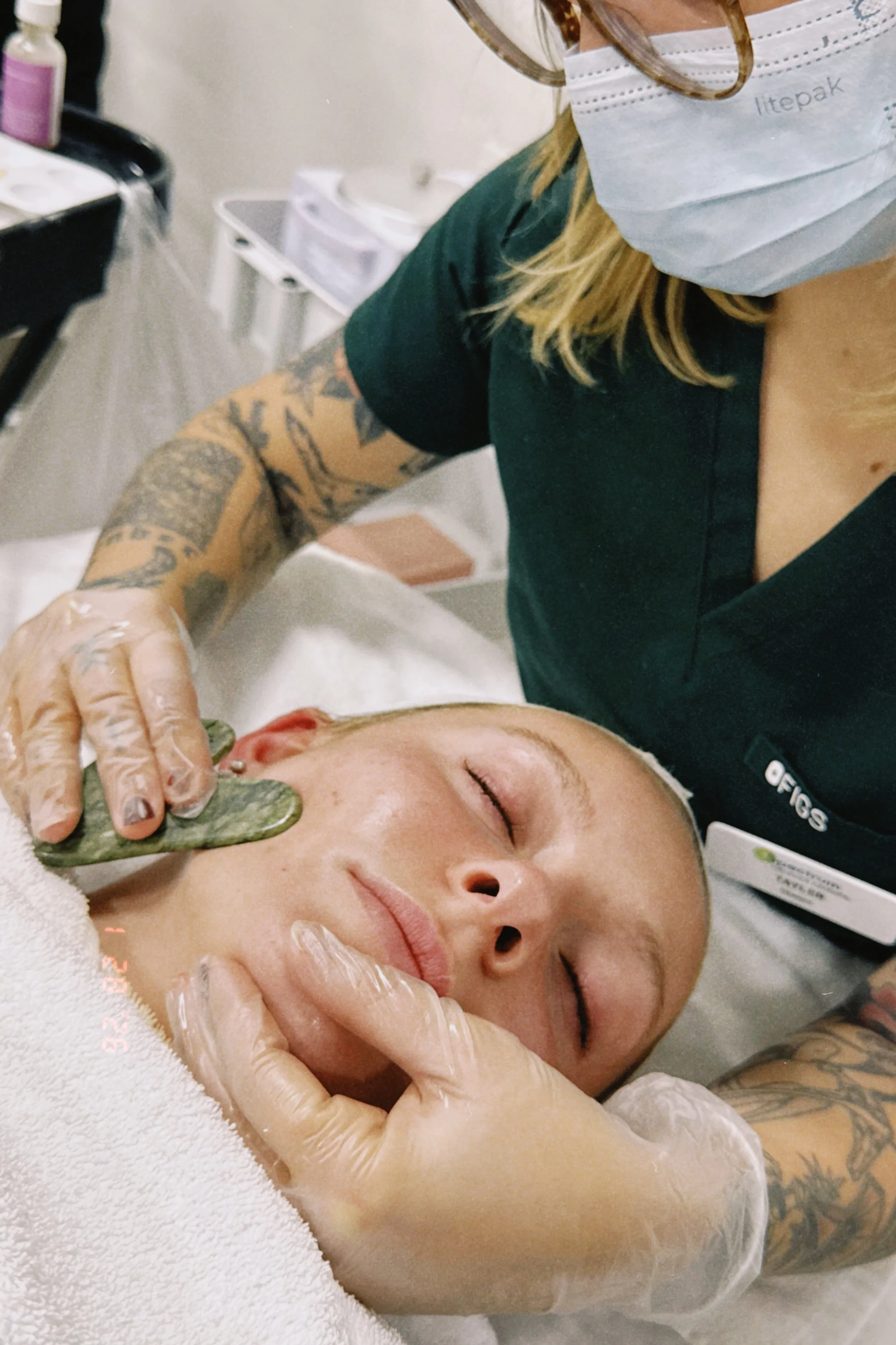 A person receiving a facial massage from a skincare professional wearing gloves in a spa or skincare clinic.