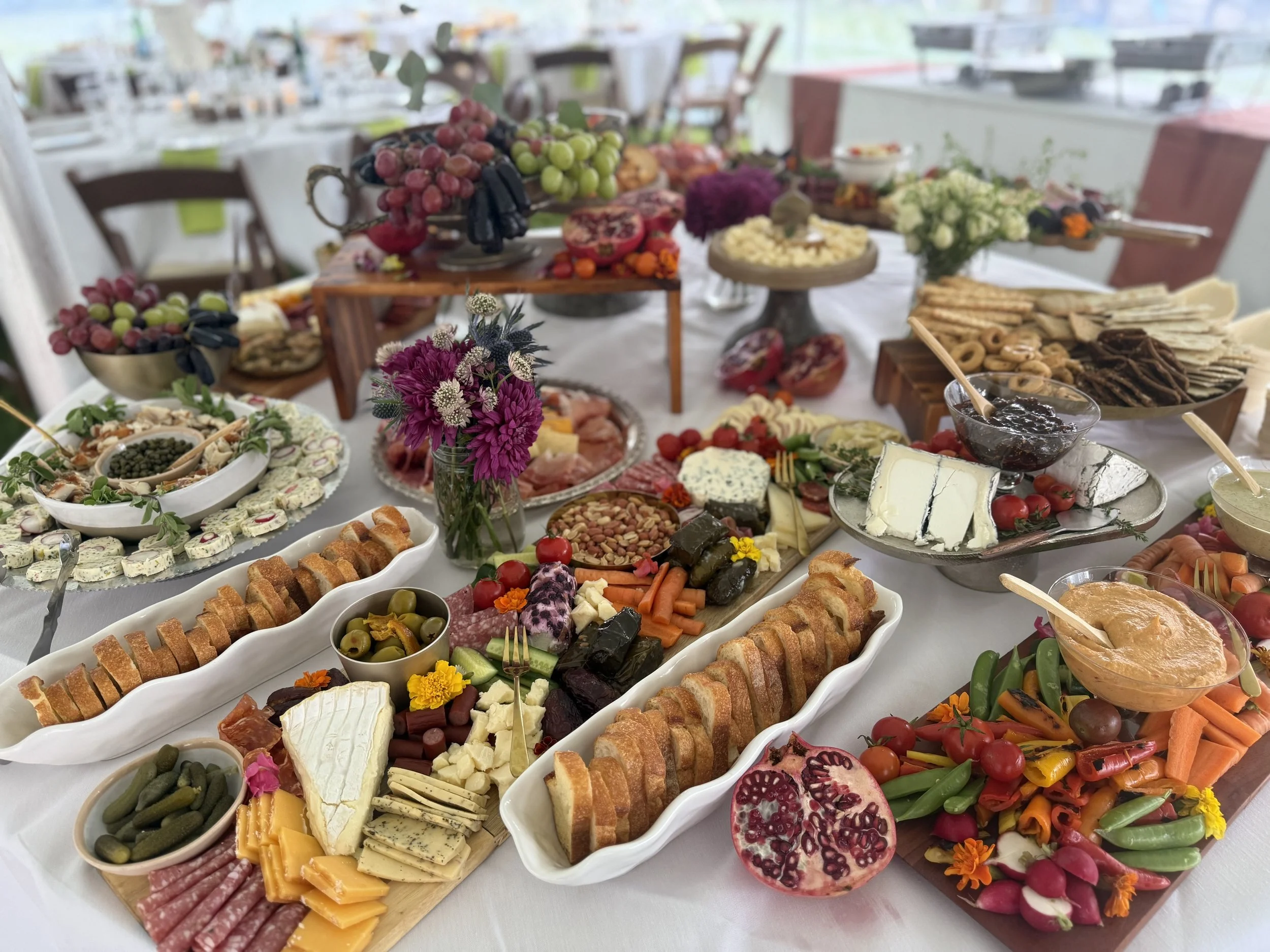 A table set with an assortment of appetizers, cheeses, fruits, vegetables, and dips, decorated with flowers for a festive gathering.